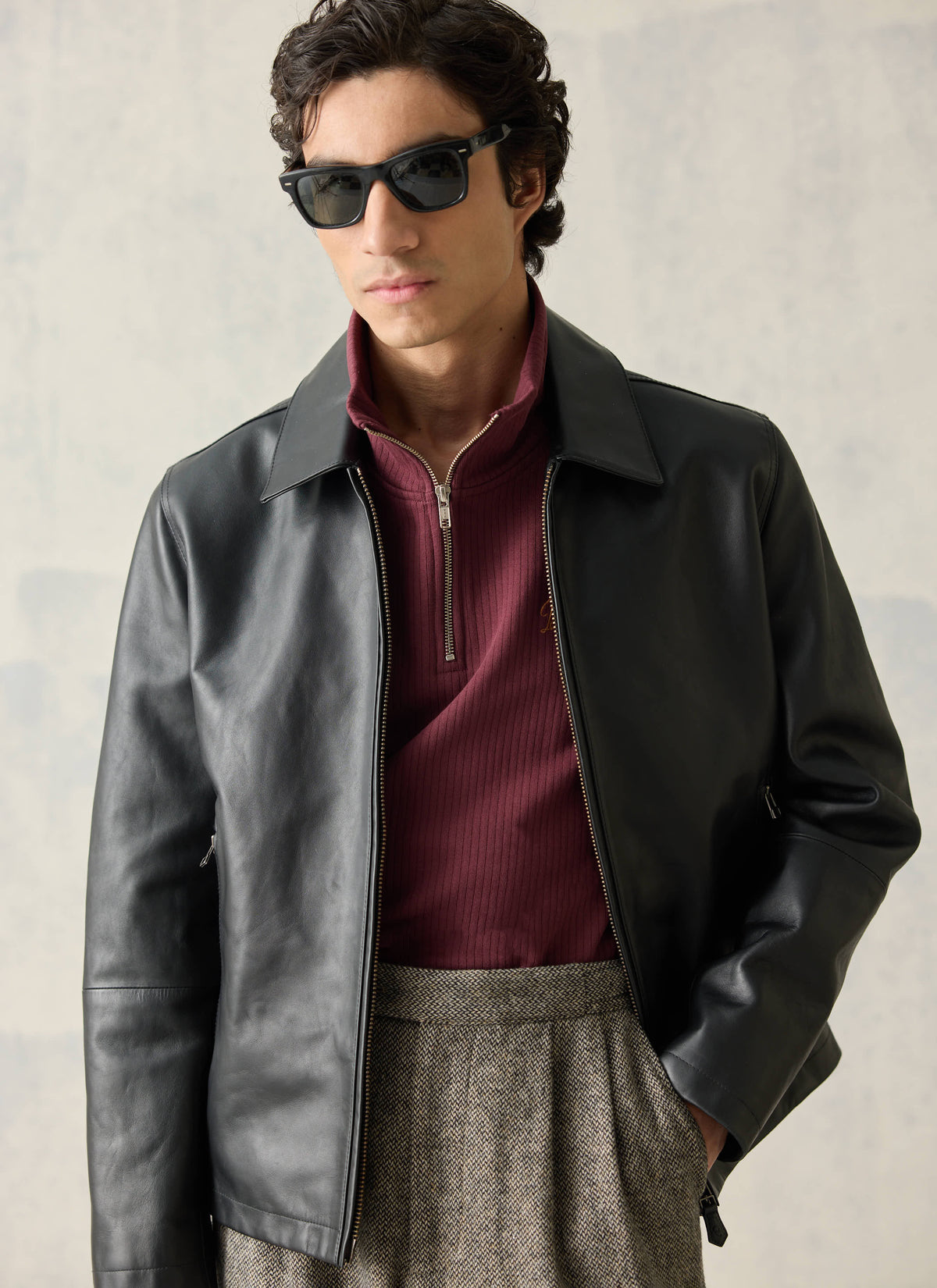 Model wearing the Percival black Turner leather jacket over a burgundy zip-neck knit and trousers with sunglasses.