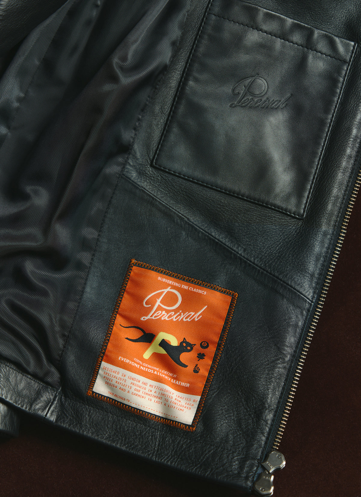 A close-up of the interior of the black Percival Turner leather jacket showing the custom internal patch label and pocket.