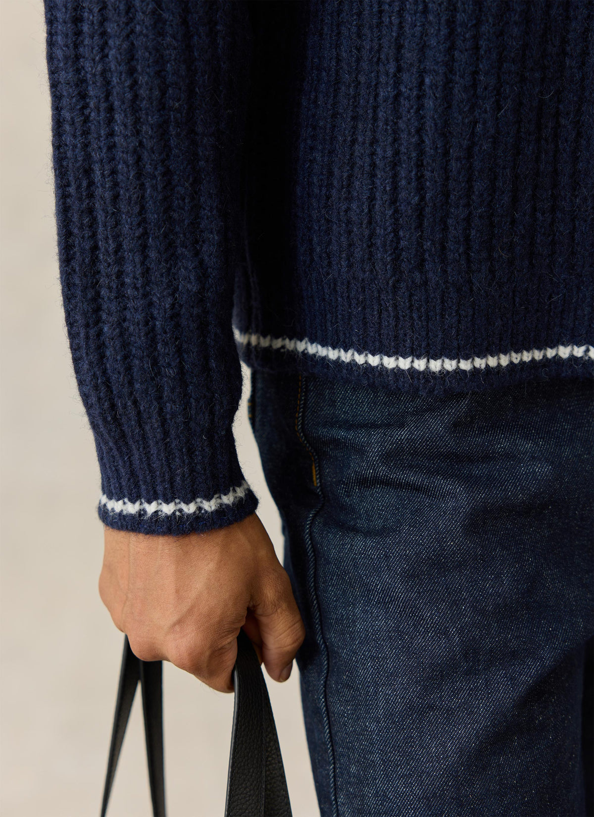 Close-up of the Percival navy V-neck jumper showing the textured rib knit, contrast hem and cuff trim, and denim trousers.