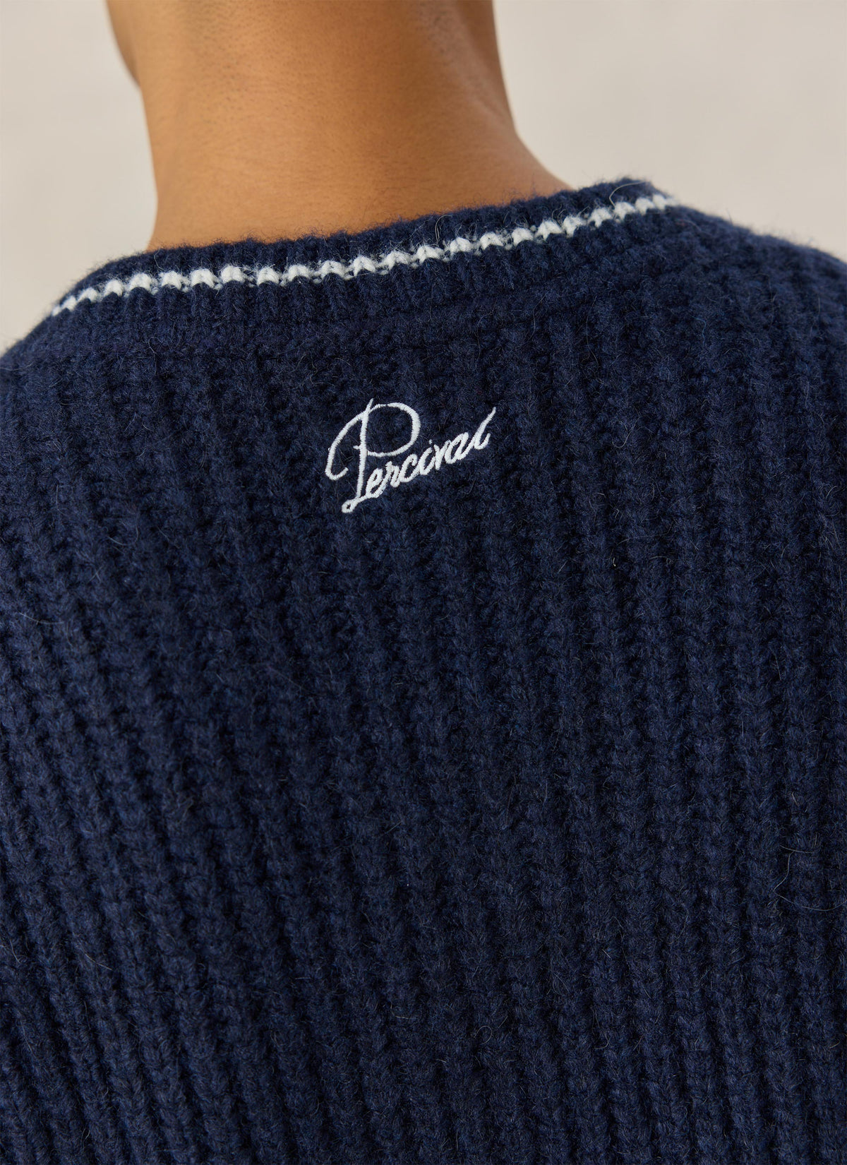 A close-up of the back of the Percival navy alpaca wool V-neck jumper showing the white embroidered script logo.