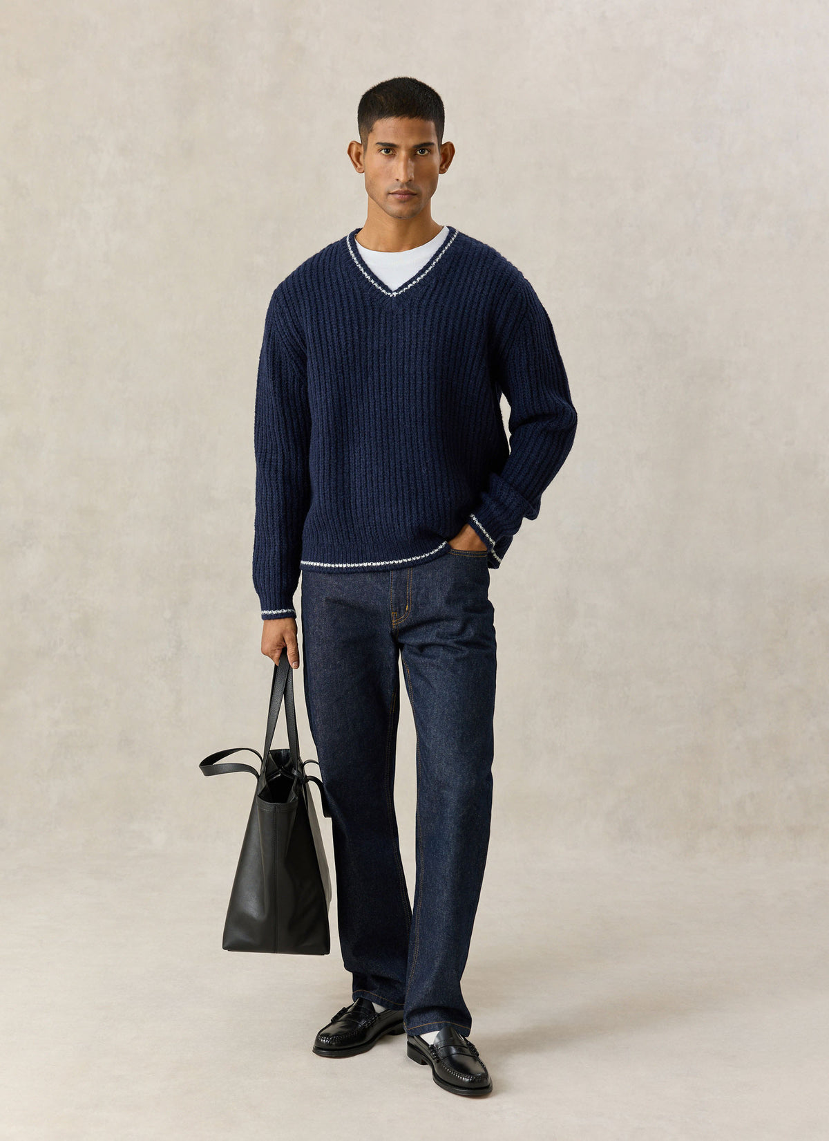 A model wearing the navy Percival Vincent V-neck knit jumper in a textured alpaca and wool blend with a black tote bag.