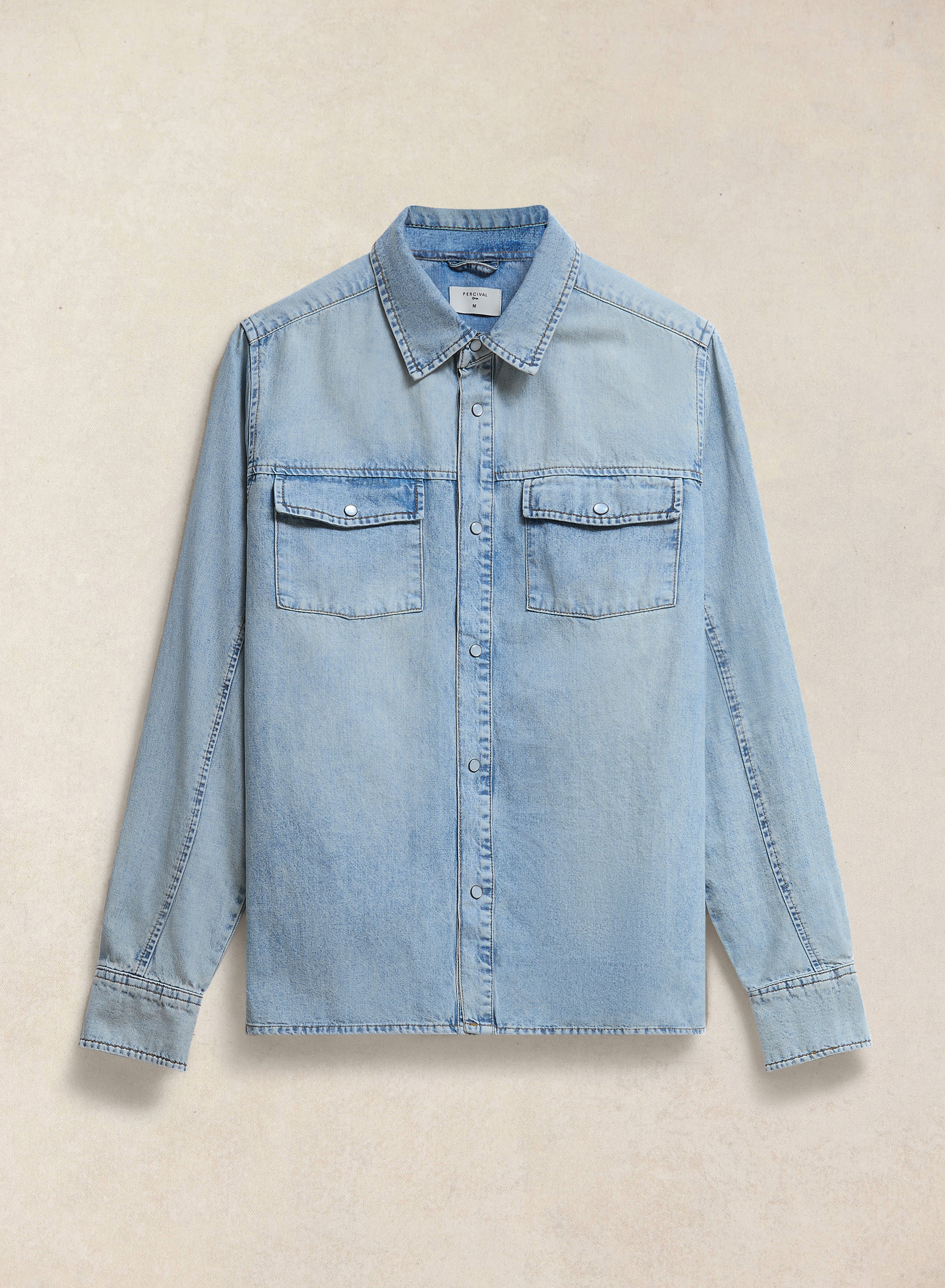 The Percival Vintage Wash Western Shirt in stone wash denim, featuring twin flap pockets and pearl buttons, flat lay.
