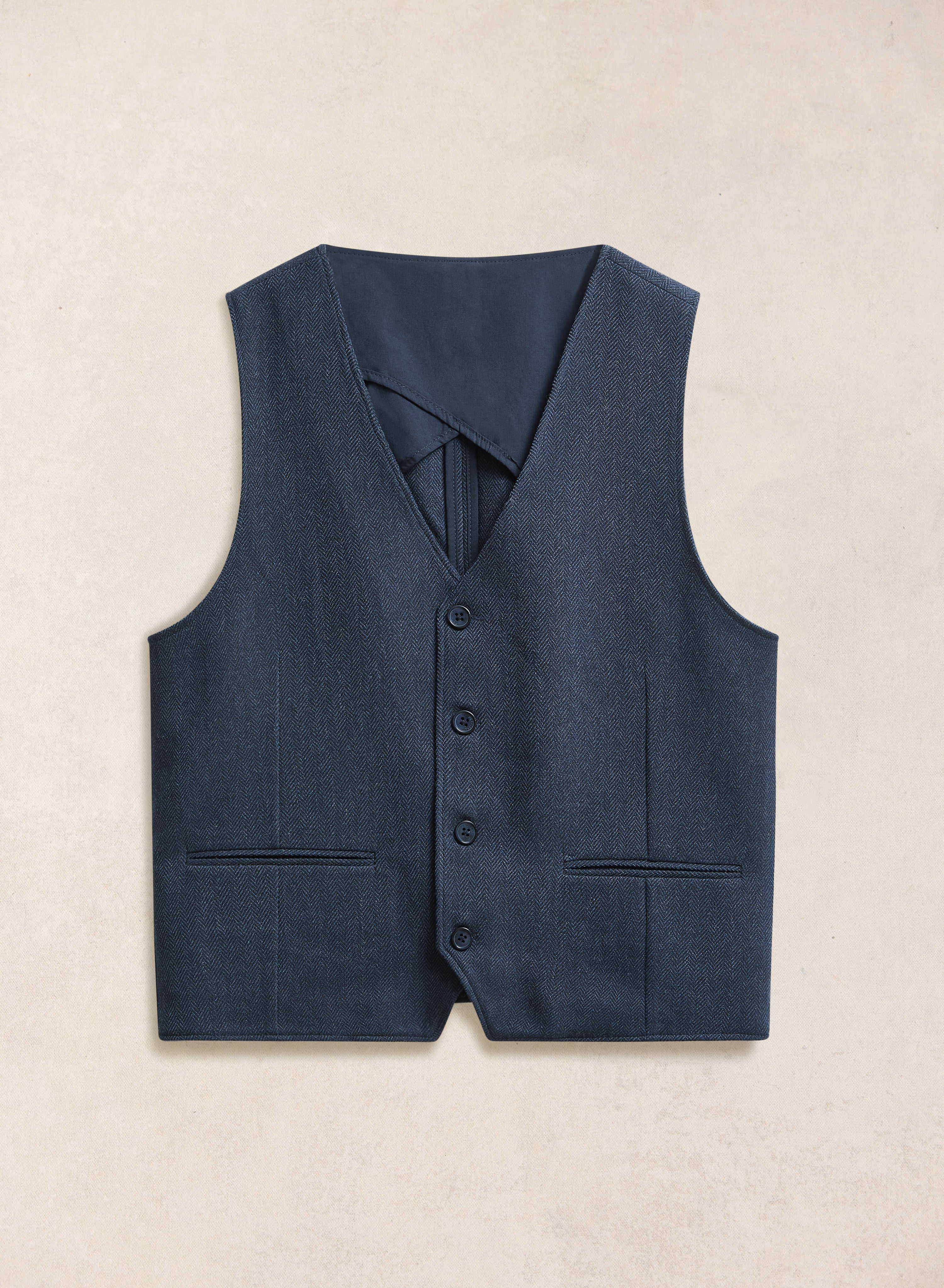 A flat lay of the Percival navy herringbone wool waistcoat, featuring a four-button front and welt pockets.
