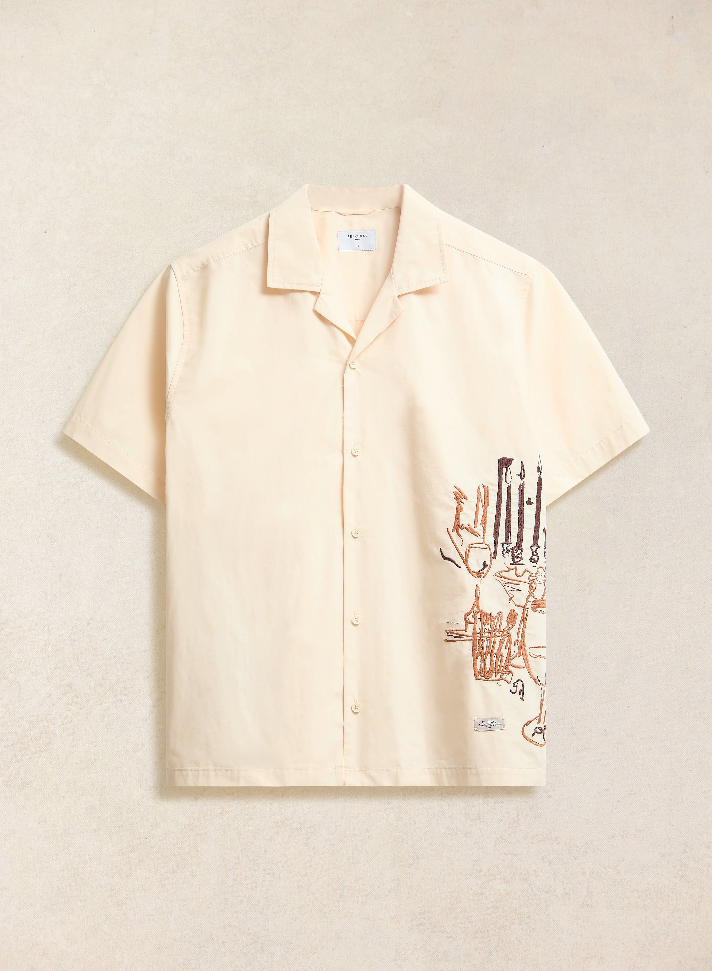 The Percival Supper Club embroidered Cuban shirt in cream, laid flat to showcase the dinner-party illustration.