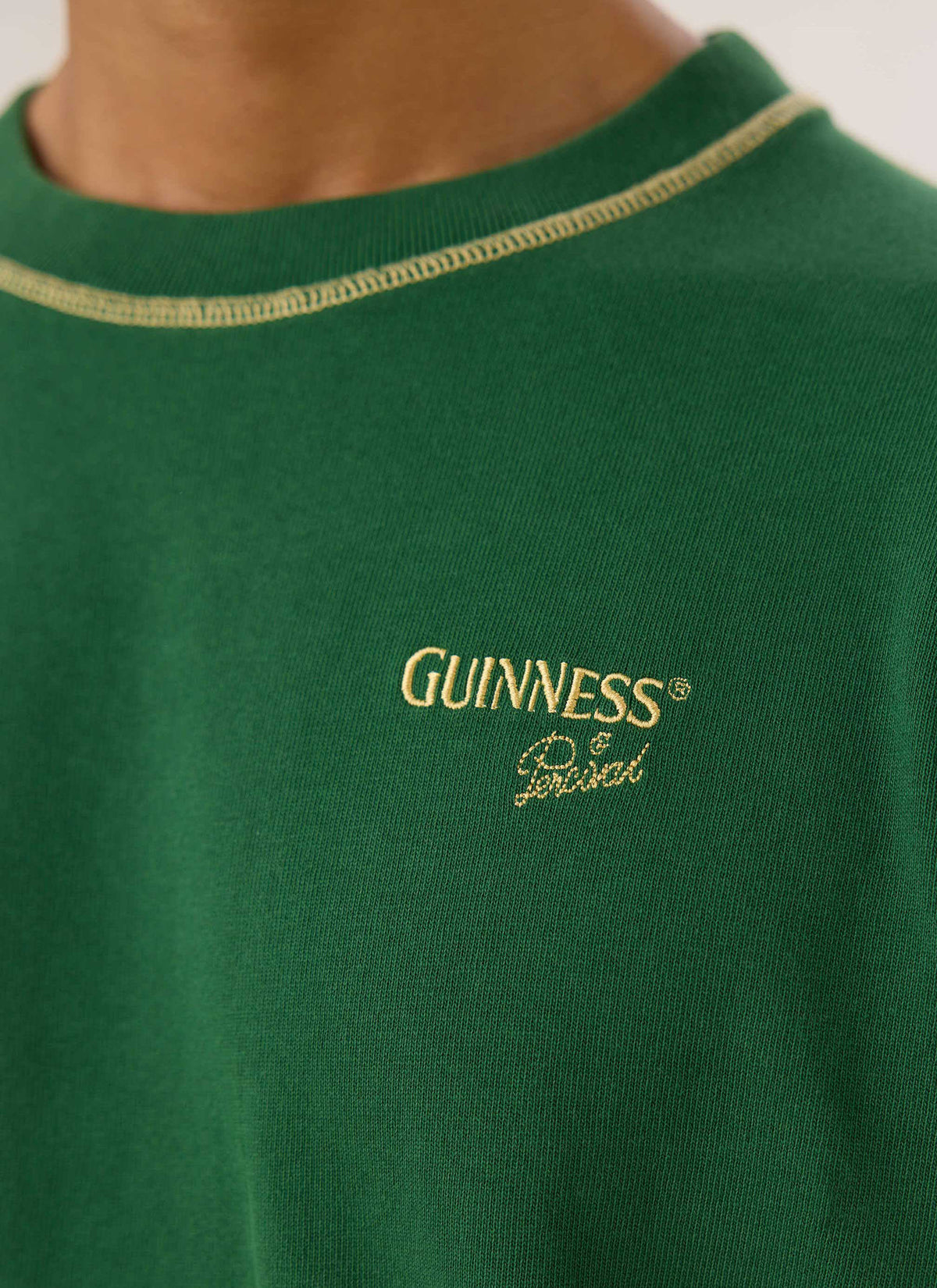 Close-up of the forest green Guinness x Percival T-shirt, highlighting the embroidered chest logo and contrast stitching.