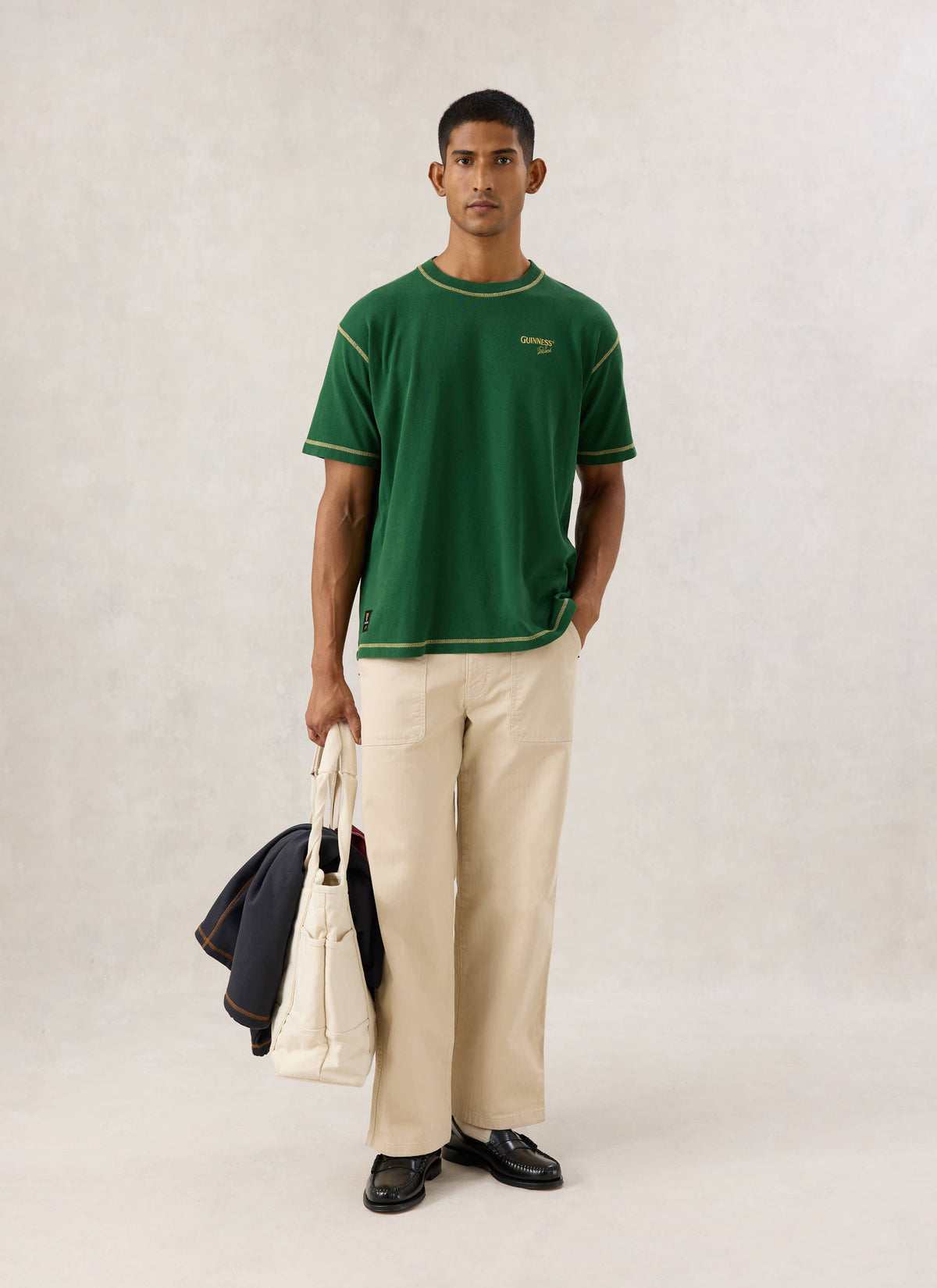 Model wearing the vintage wash forest green oversized T-shirt from Guinness x Percival, paired with cream trousers.