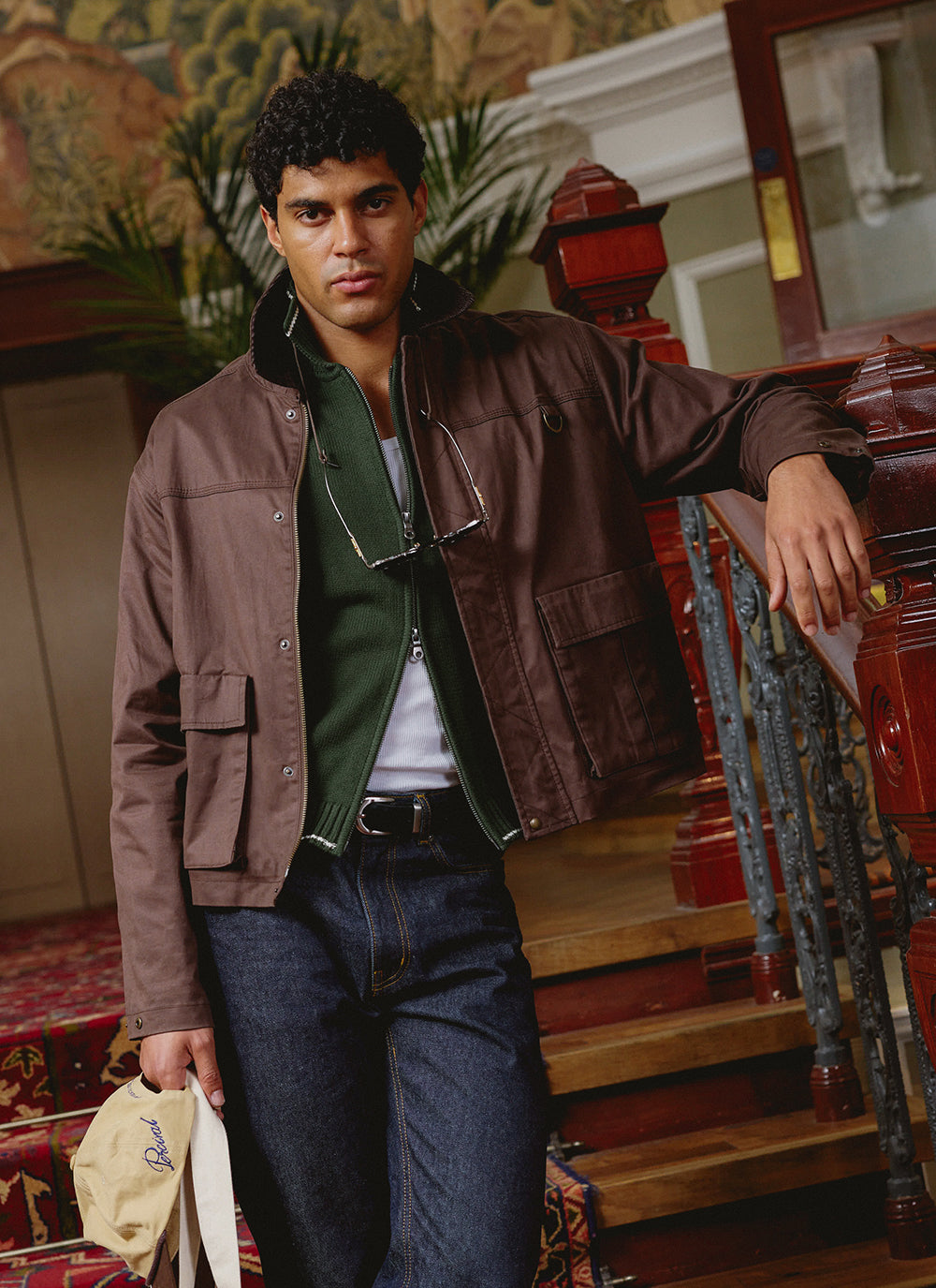 A model wearing the Percival espresso brown wax zip jacket, layered over a forest green zip cardigan and dark raw jeans.