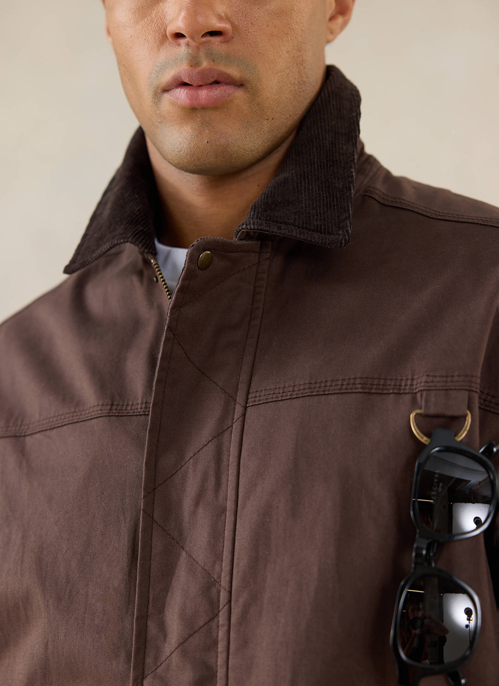 Close-up of a model wearing the Percival brown wax jacket in espresso with sunglasses clipped to the pocket.
