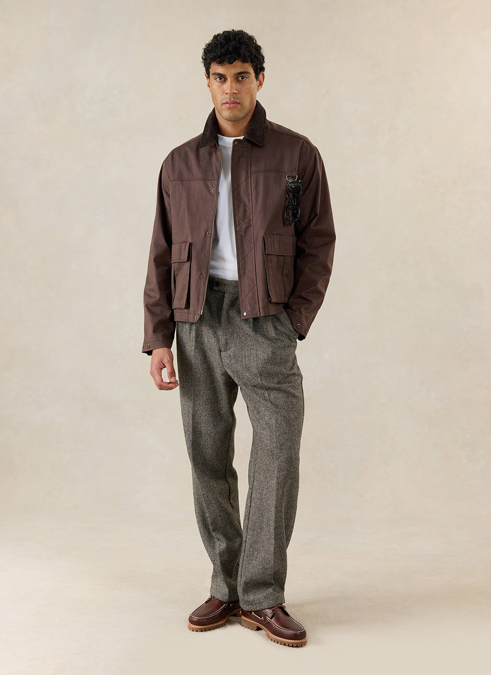 A model wears the Percival brown waxed zip jacket in espresso over a white t-shirt and grey patterned trousers.
