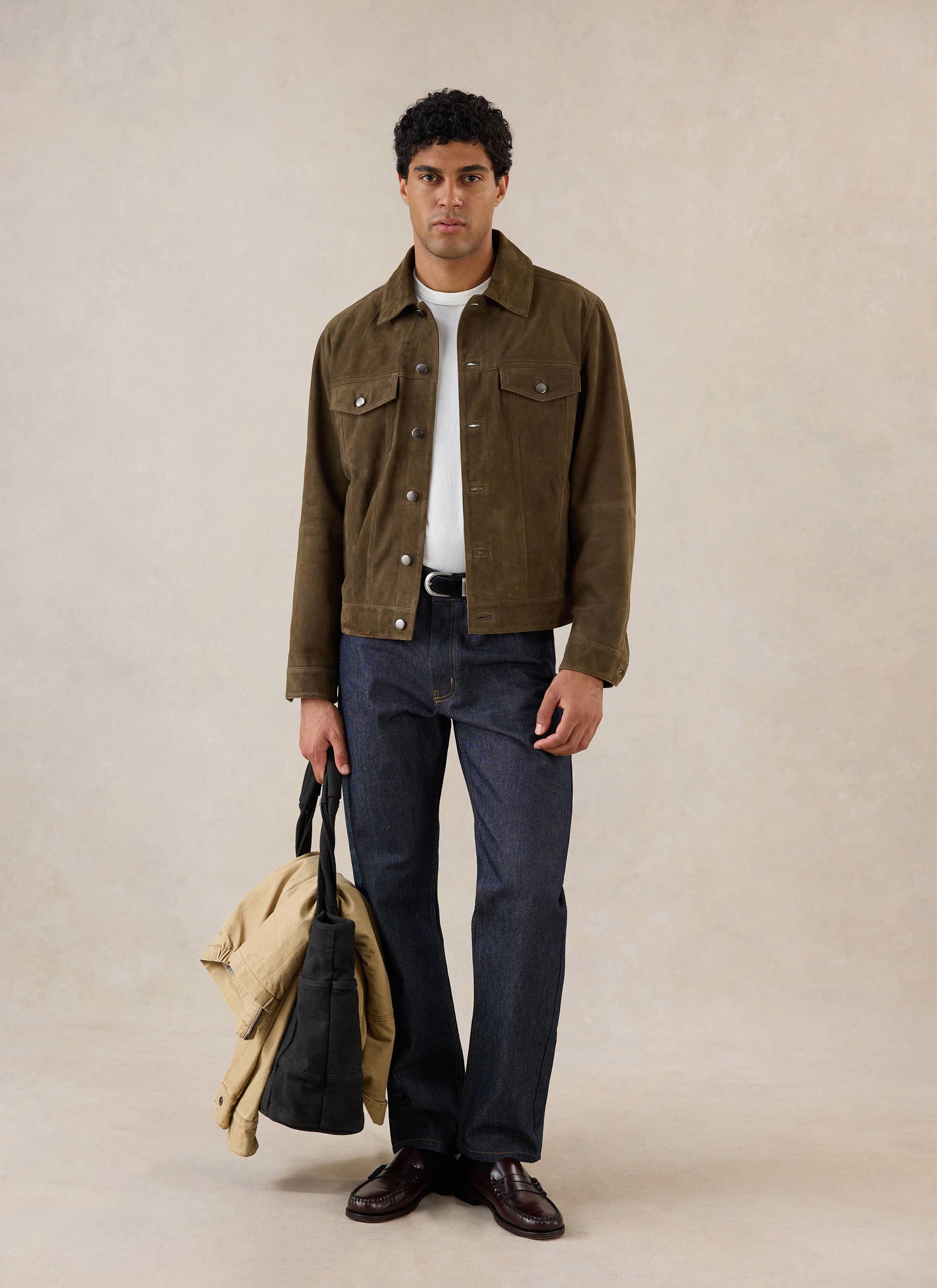 A model wears the olive Percival suede western jacket over a white t-shirt and dark jeans while holding a tote bag.