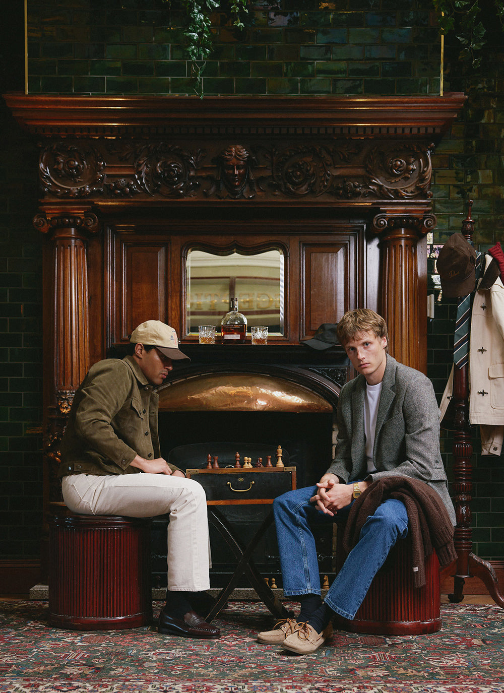 Two models by a fireplace wearing Percival outerwear, including an olive suede western jacket and a birdseye wool blazer.