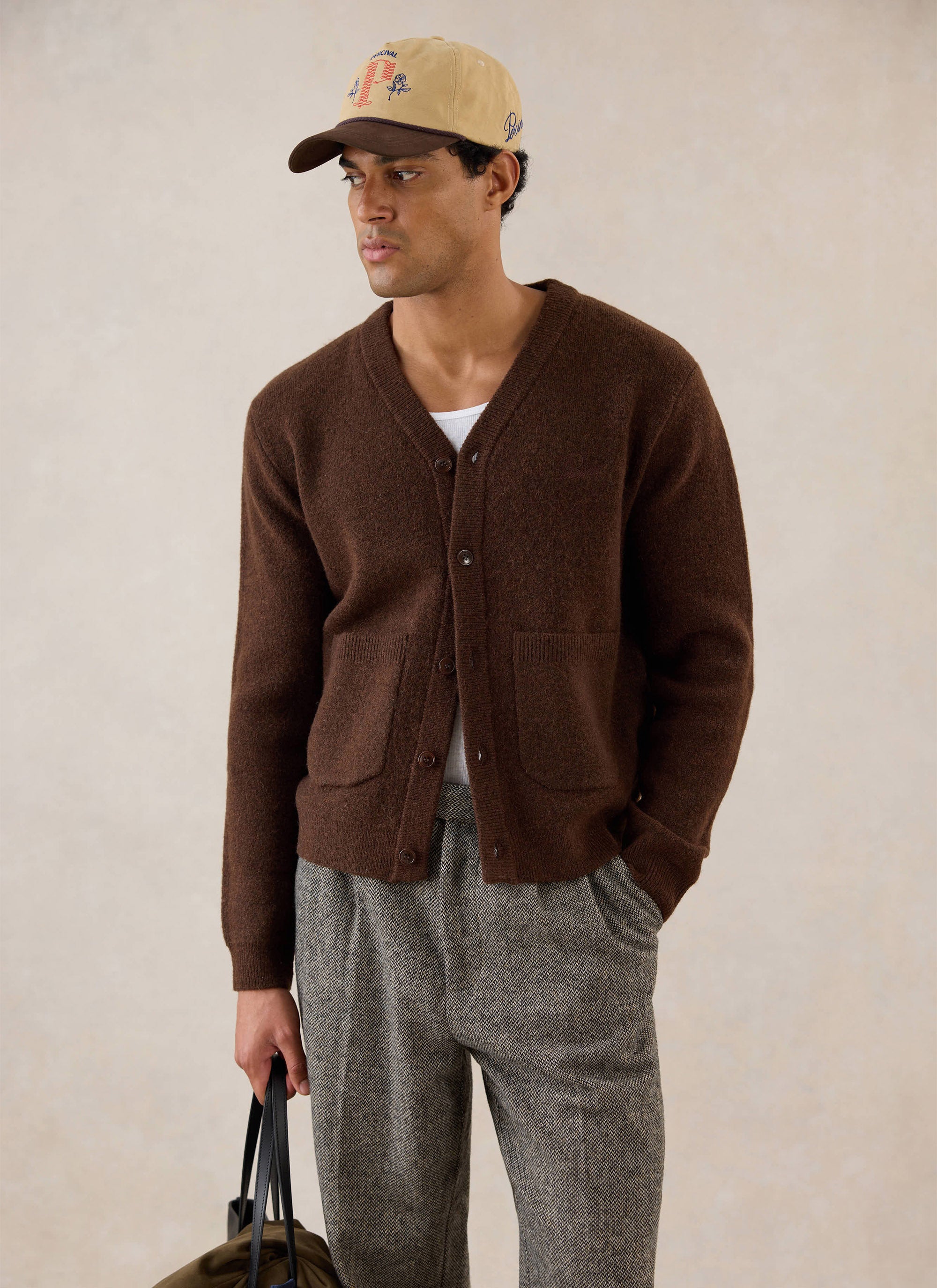 A model wears the Percival espresso brown mohair wool blend cardigan with a baseball cap and patterned trousers.