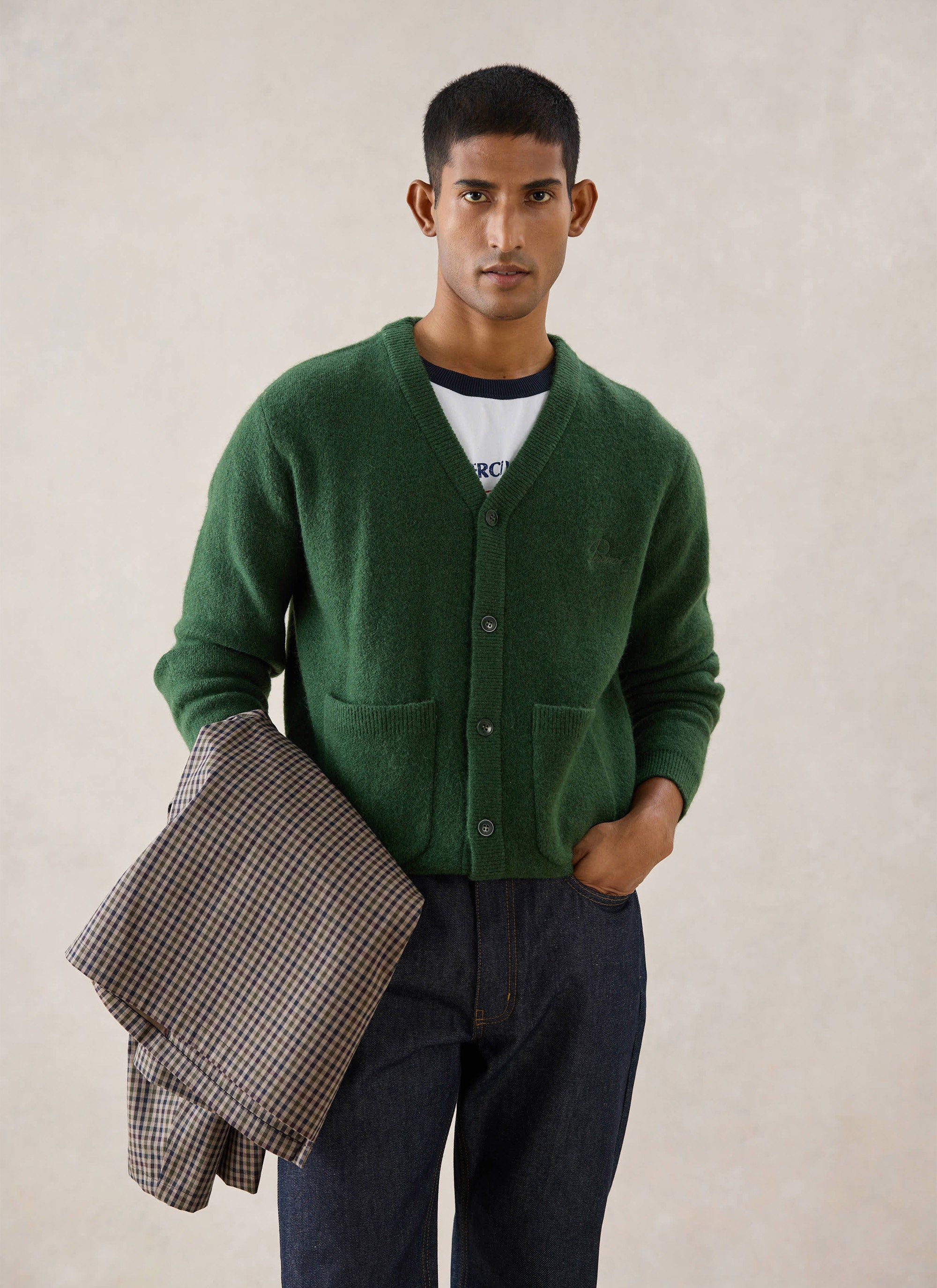 A model wearing the Percival forest green mohair wool blend White Glove cardigan, holding a patterned jacket.