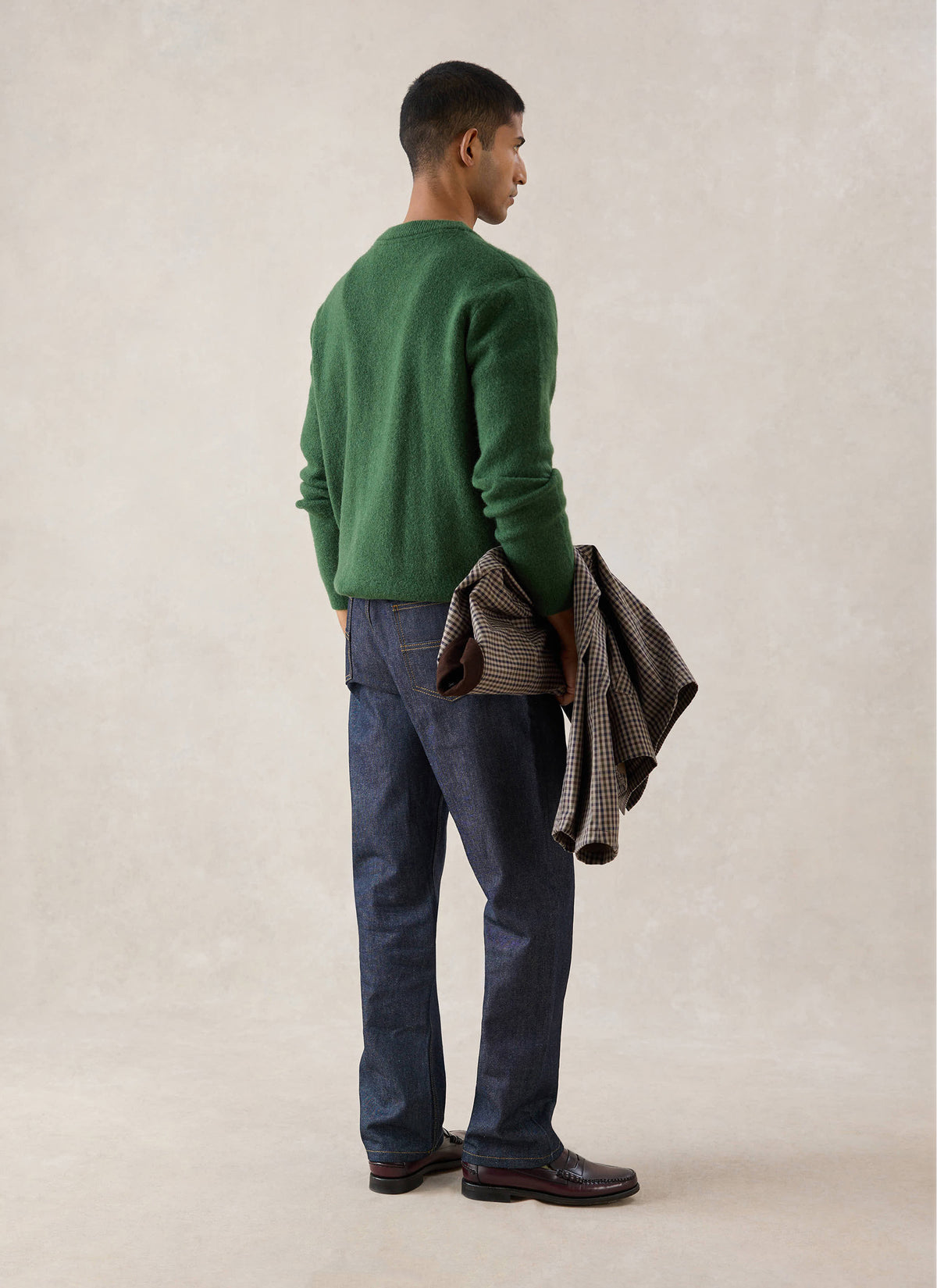 A model from the back wearing the forest green Percival mohair wool blend cardigan with jeans and holding a jacket.