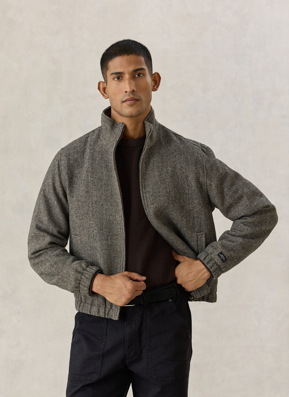 A model wearing the Percival Wilde Harrington jacket in birdseye grey wool blend, featuring a stand collar and zip.