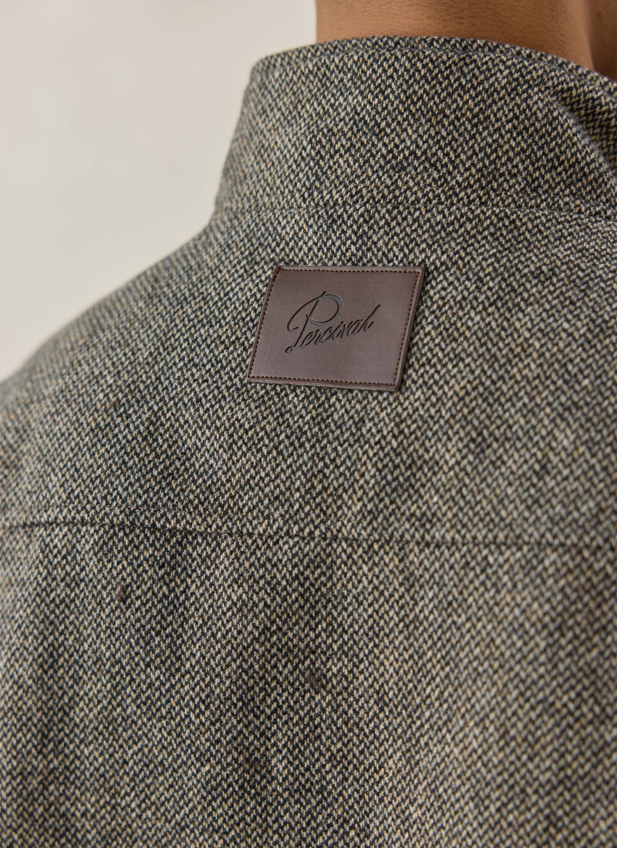 A close-up of the grey birdseye wool Percival Wilde Harrington jacket showing the back collar and branded leather patch.