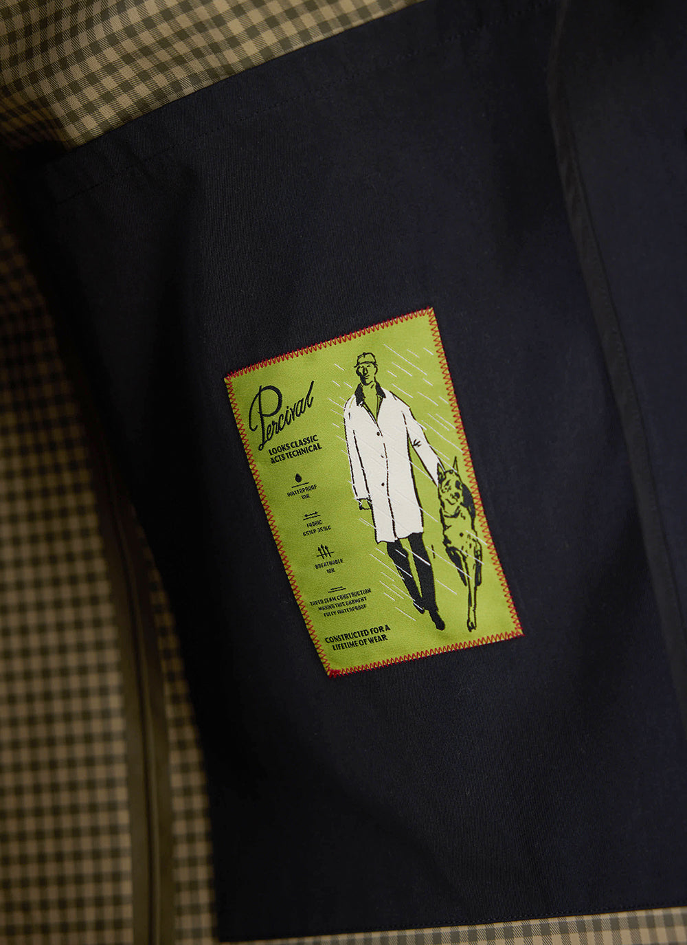 A close-up of the green technical detail label on the black Wilson Long Trench Coat from Percival.