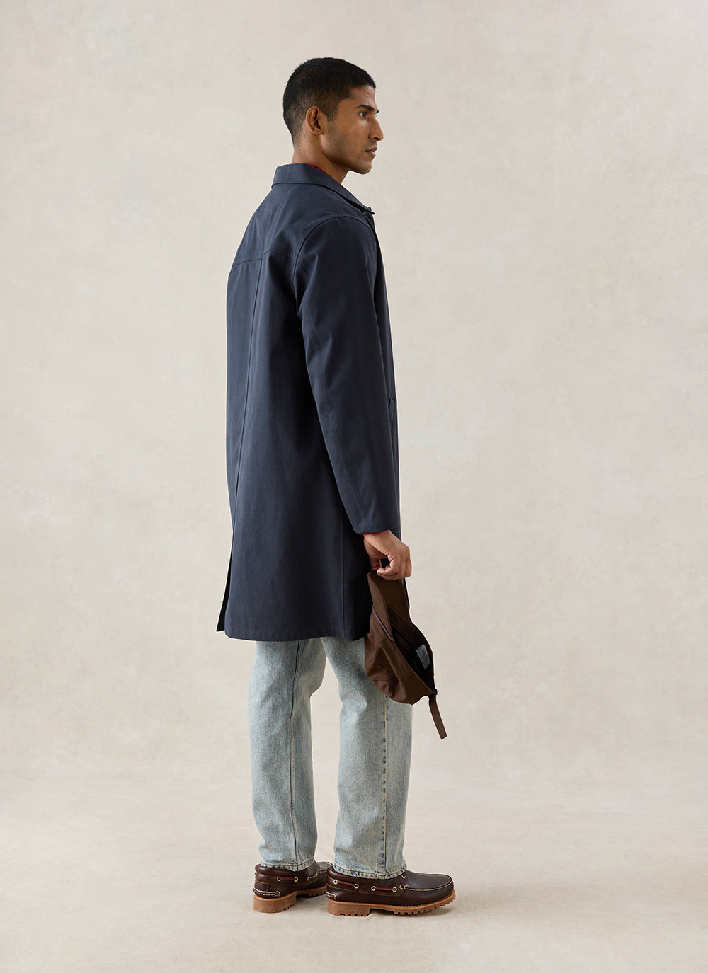 A model wears the midnight Percival Wilson Long Trench Coat from the side, styled with light wash jeans and brown shoes.