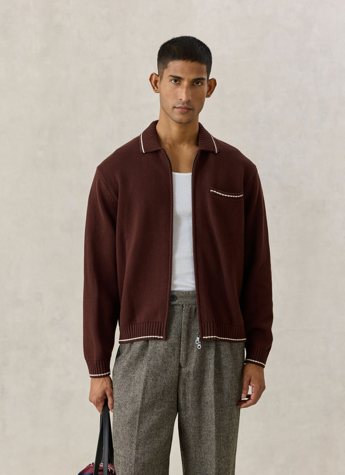 A model wearing the Percival Gardner zip cardigan in espresso brown with contrast tipping over trousers.