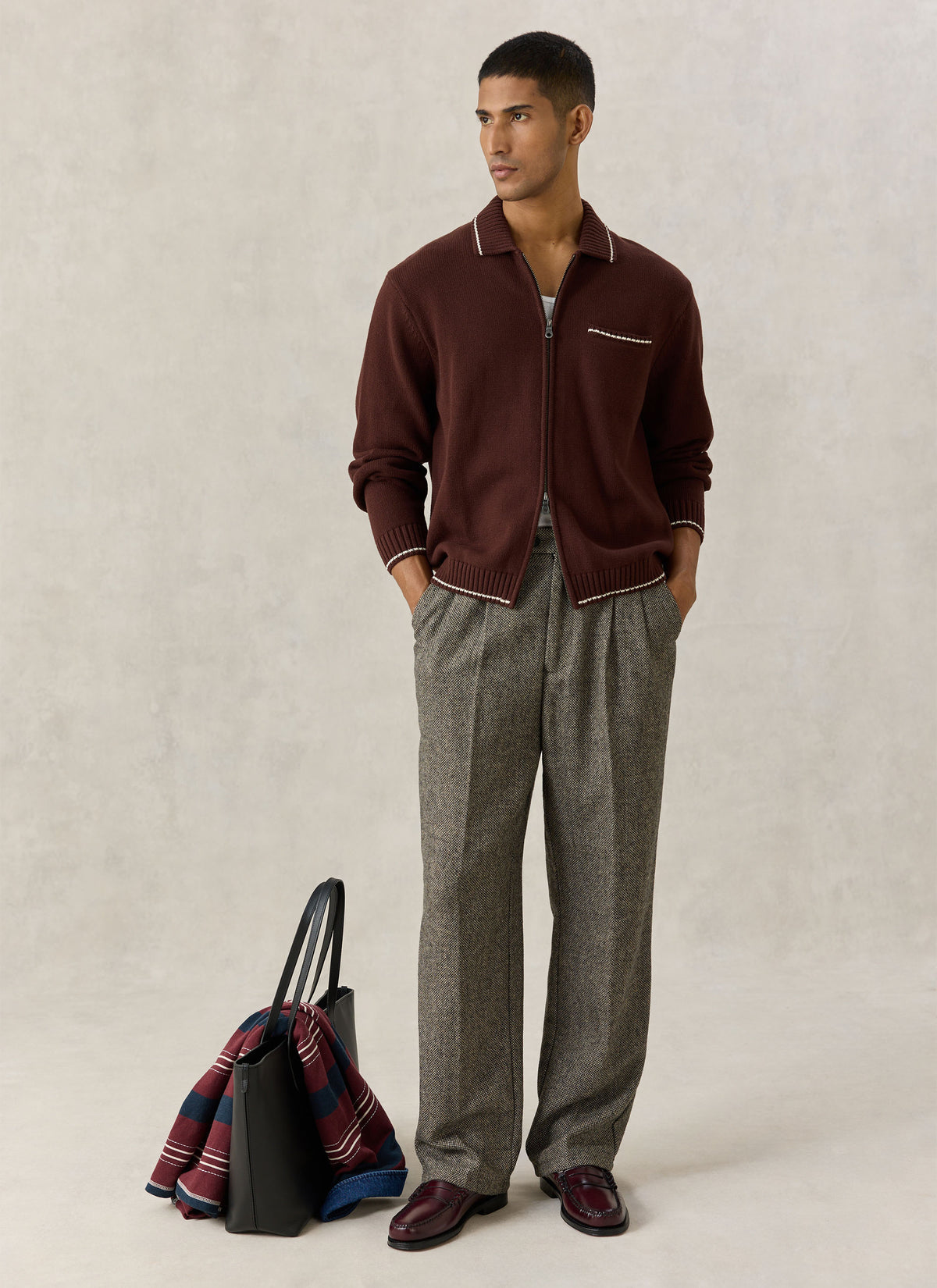 A model wearing the Percival Gardner zip cardigan in espresso brown with patterned trousers and a leather tote bag.