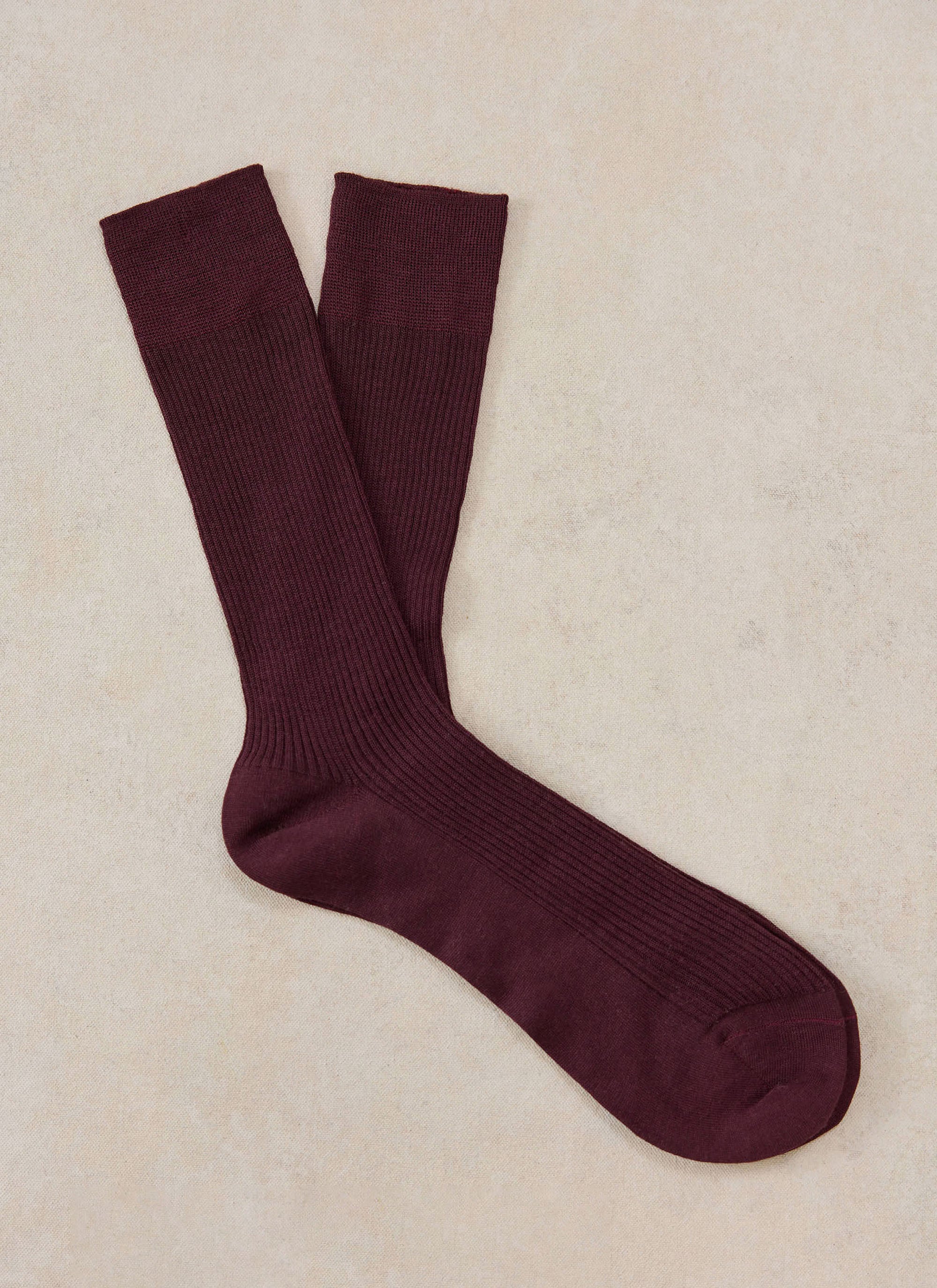 A pair of merlot merino wool socks from Percival laid flat on a neutral background.