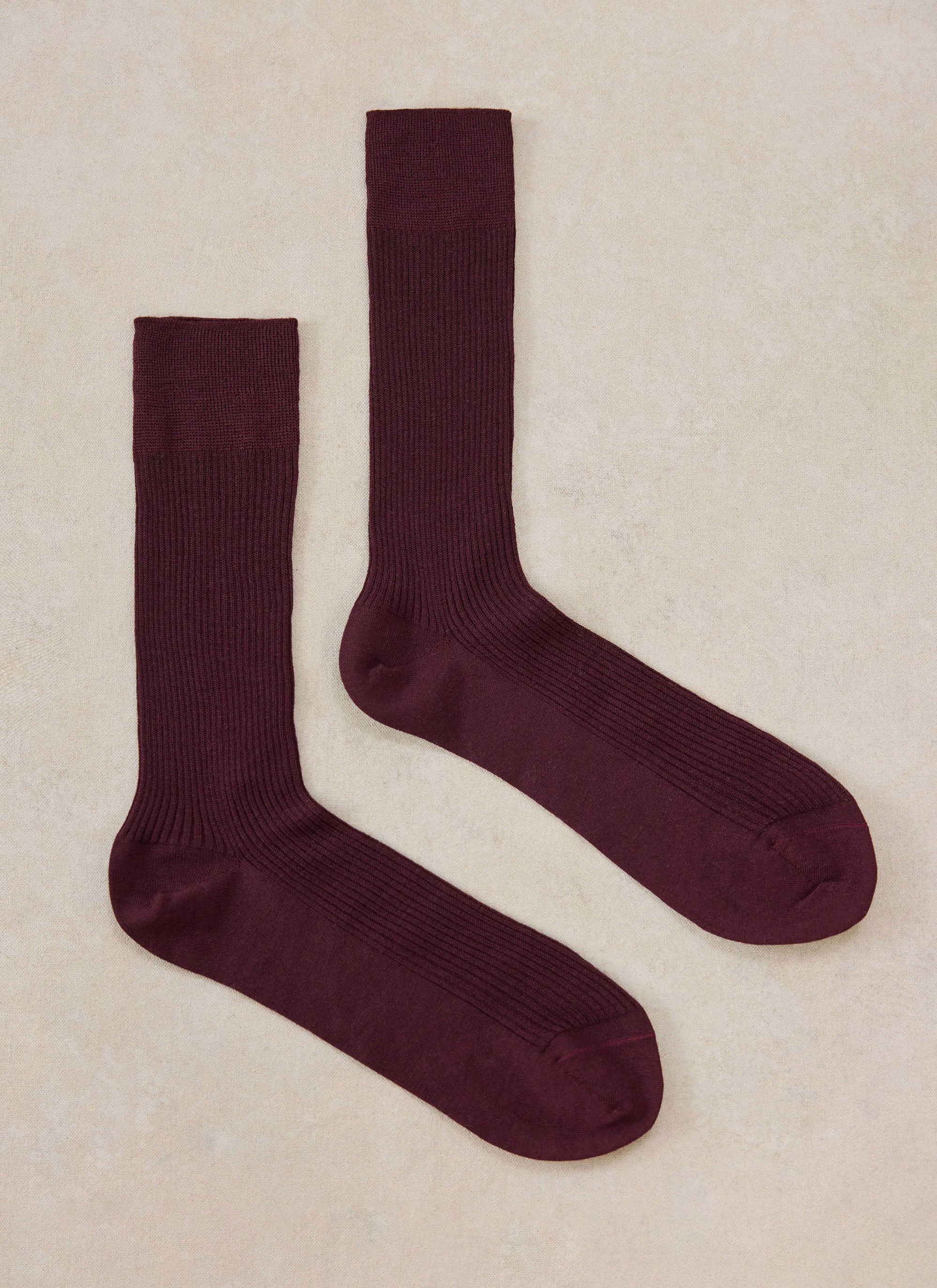A pair of merlot merino wool socks from Percival laid flat on a neutral background.