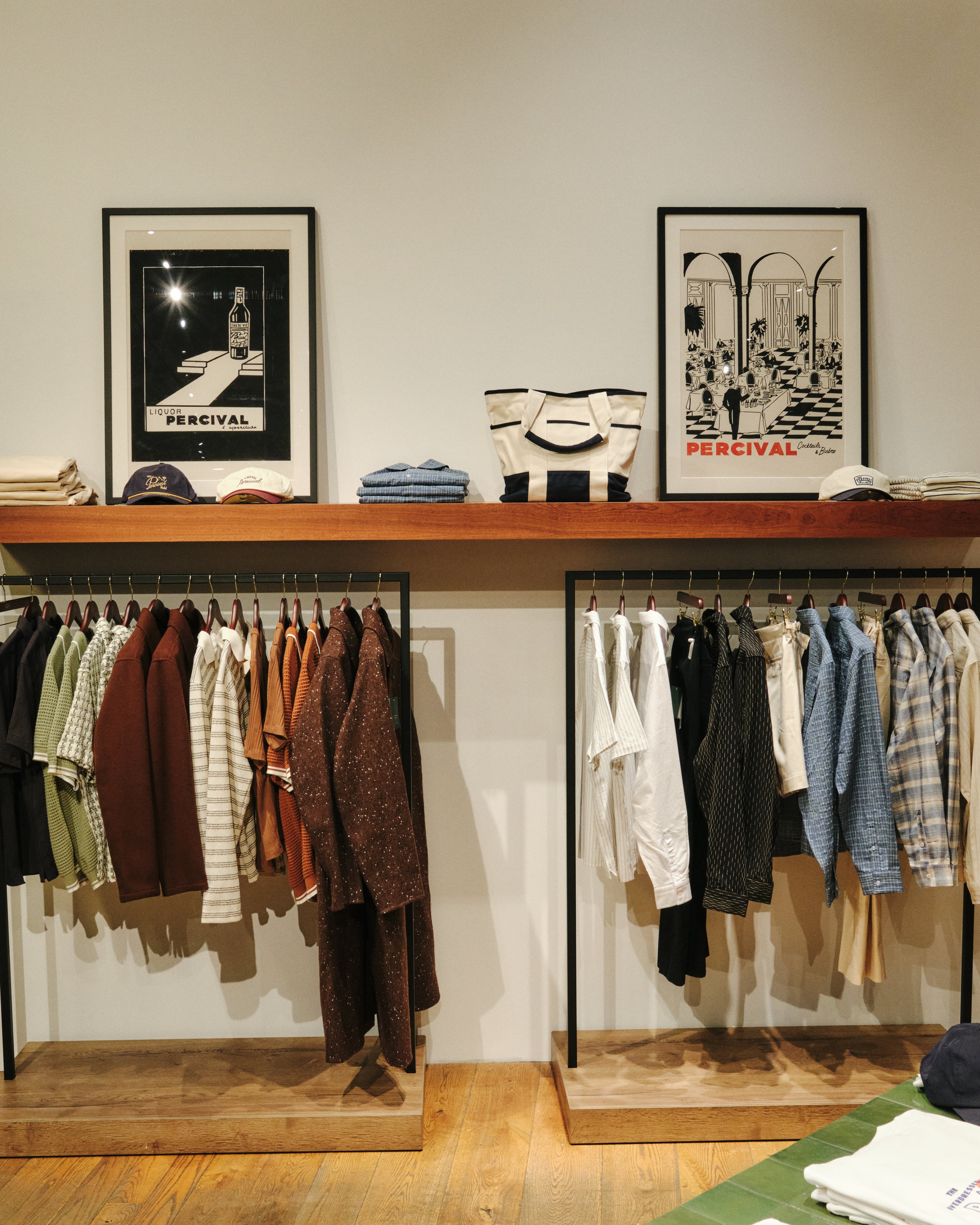 Menswear clothing display featuring shirts on hangers alongside framed art prints at the Percival pop-up store in Selfridges Birmingham.