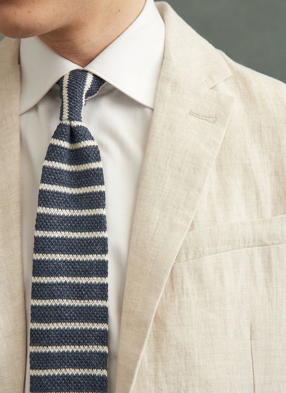 Close up of a model wearing the Percival navy marl and white stripe linen tie with a cream linen suit jacket.