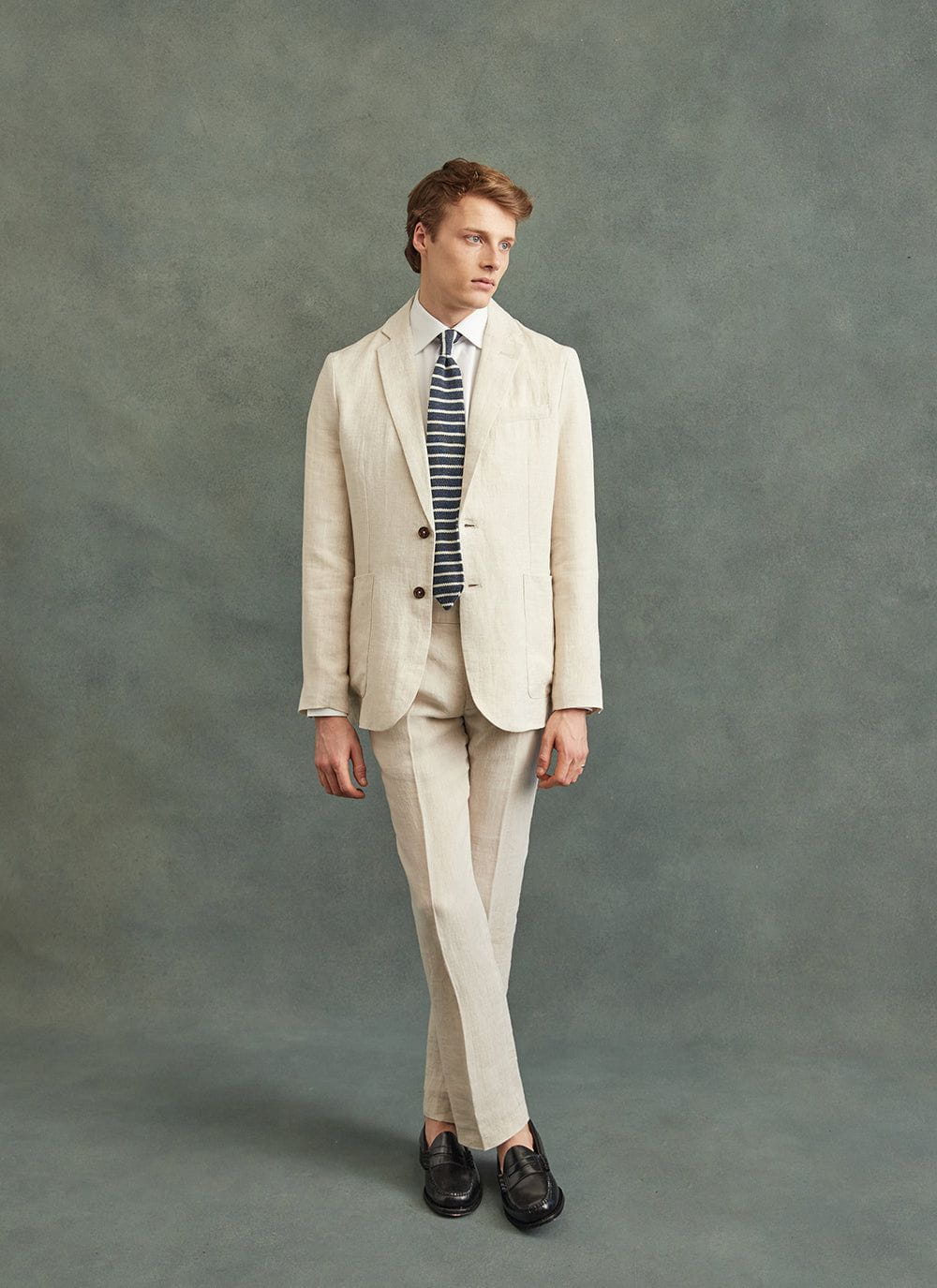 A model wears a Percival navy and white striped linen tie, styled with a cream linen suit and white shirt.