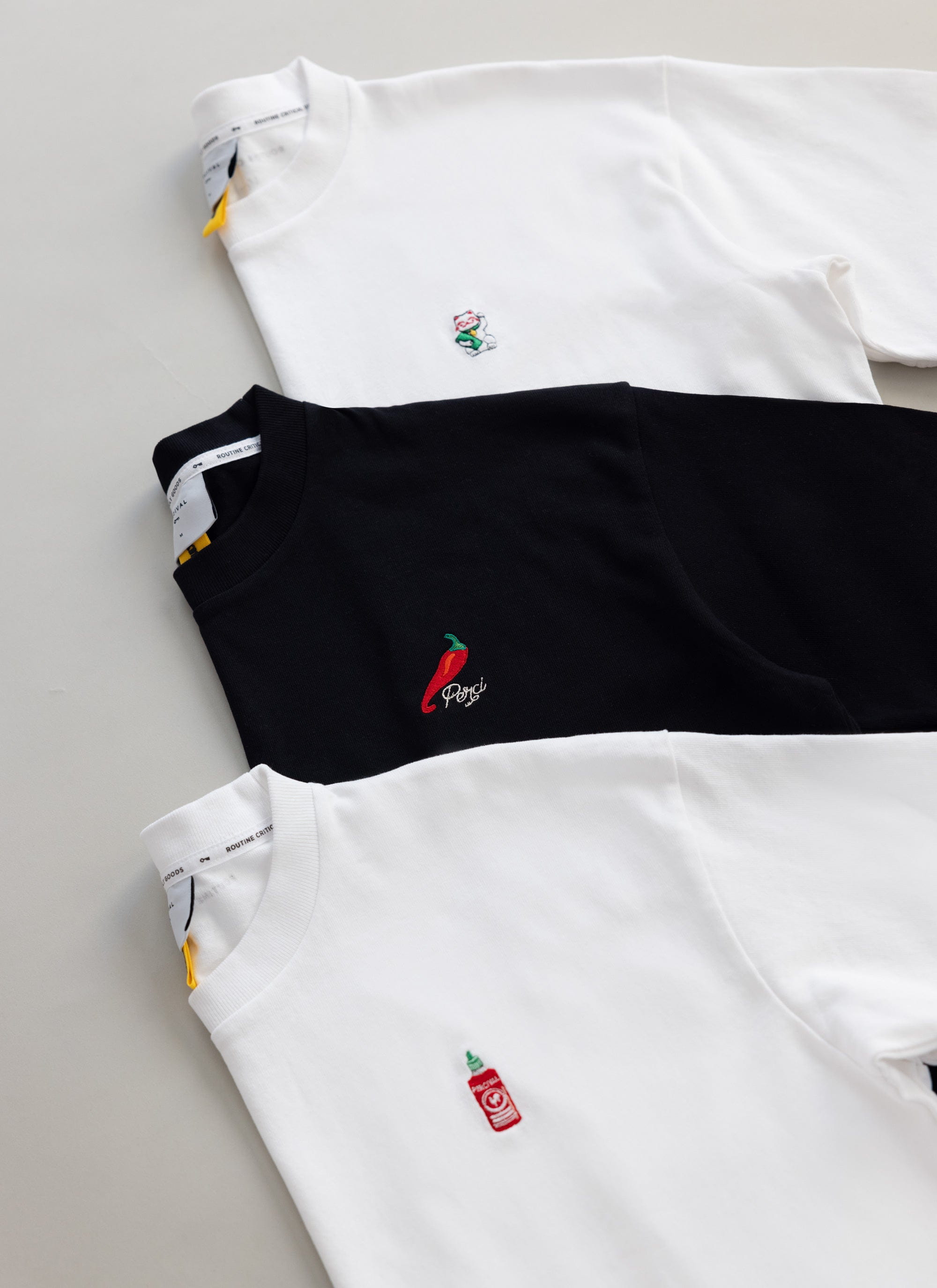 The exclusive black Percival Loyalty T-shirt with chilli embroidery, displayed with two other tees from the collection.