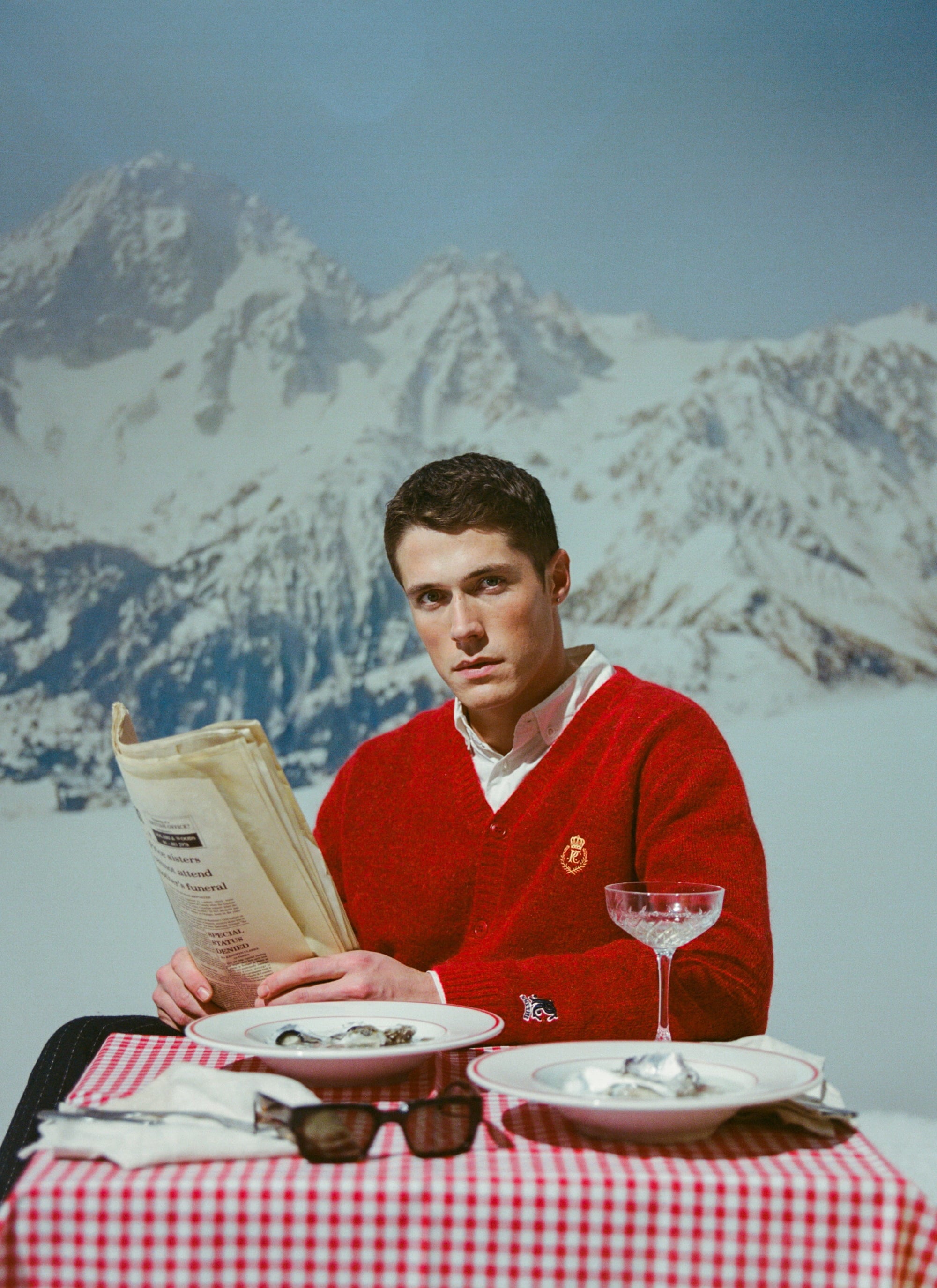 A model wears the red Champion x Percival White Glove knitted cardigan while enjoying après-ski with a snowy mountain view.