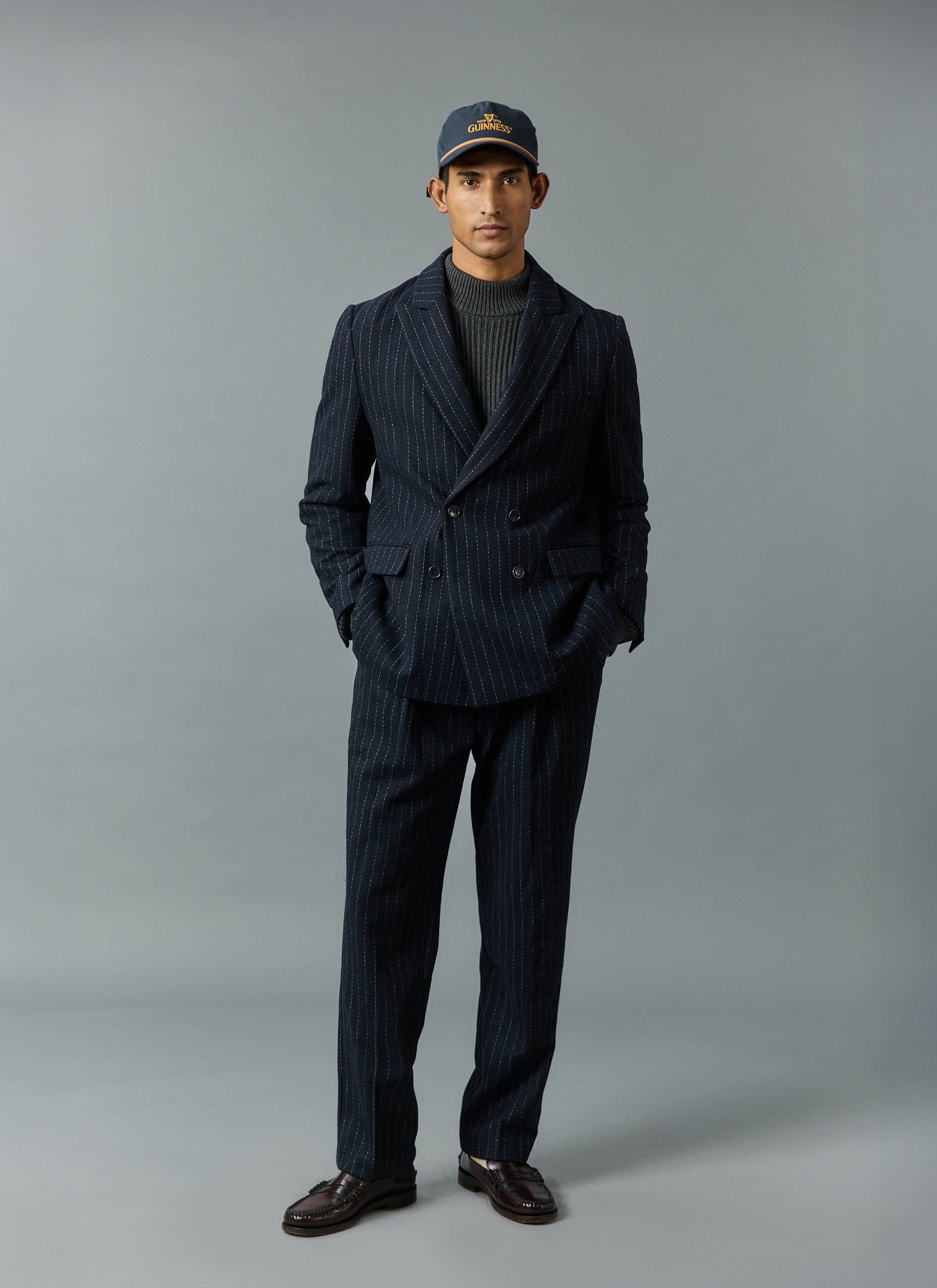 A model wears the Percival navy Textured Stripe suit, styled casually with a grey roll neck and a baseball cap.