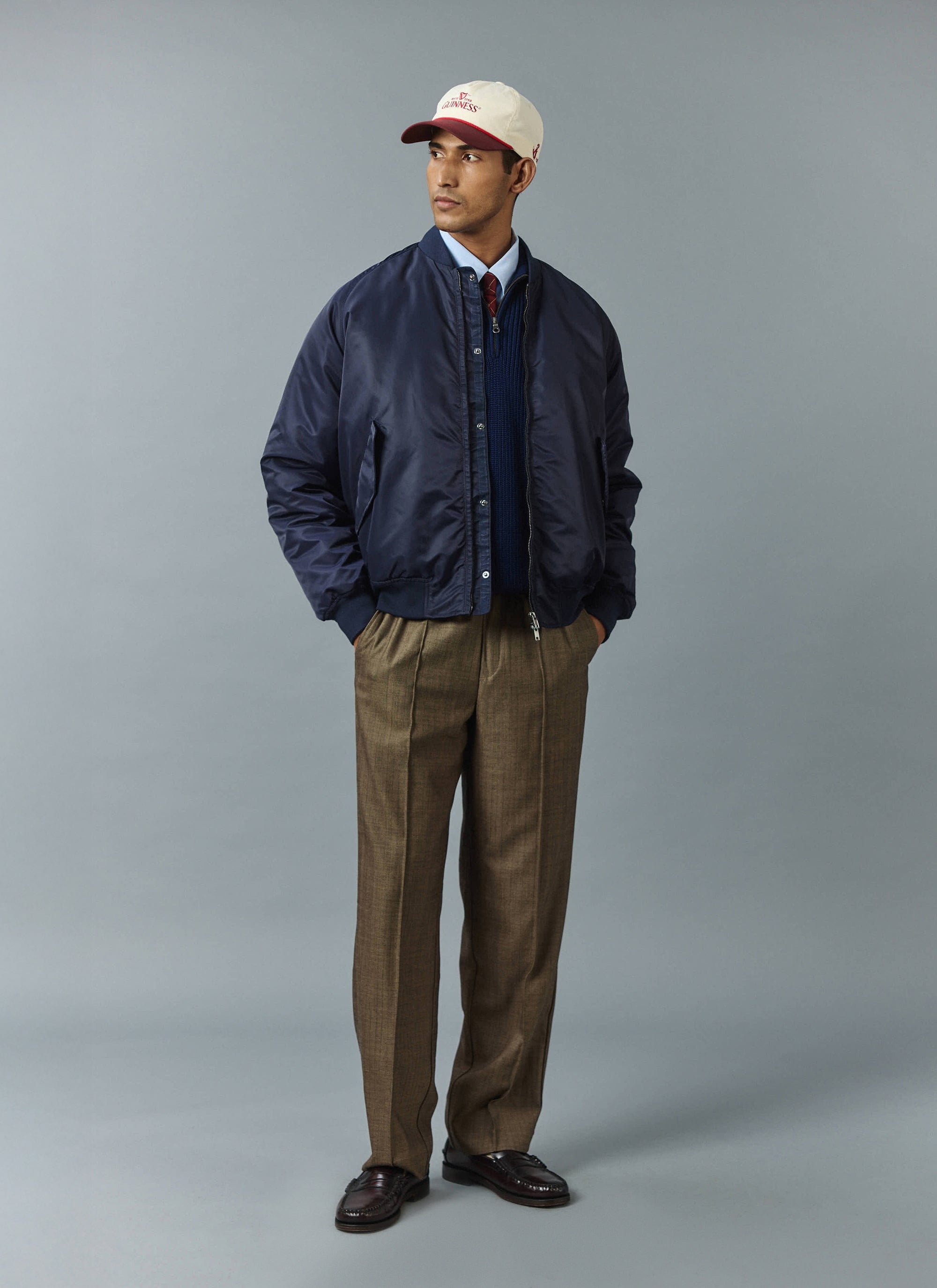 A model wears the Percival navy nylon bomber jacket with oak herringbone wool trousers against a grey studio background.