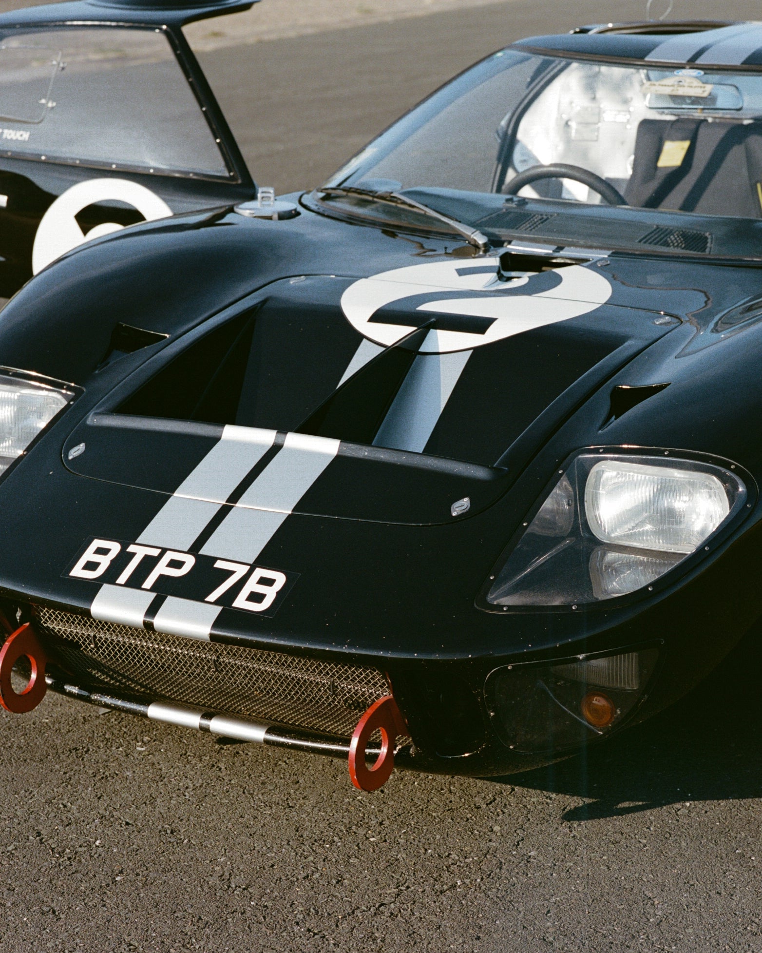 A black Ford race car with white racing stripes, a large white number 2 on the hood, and the license plate BTP 7B, photographed outdoors on asphalt.