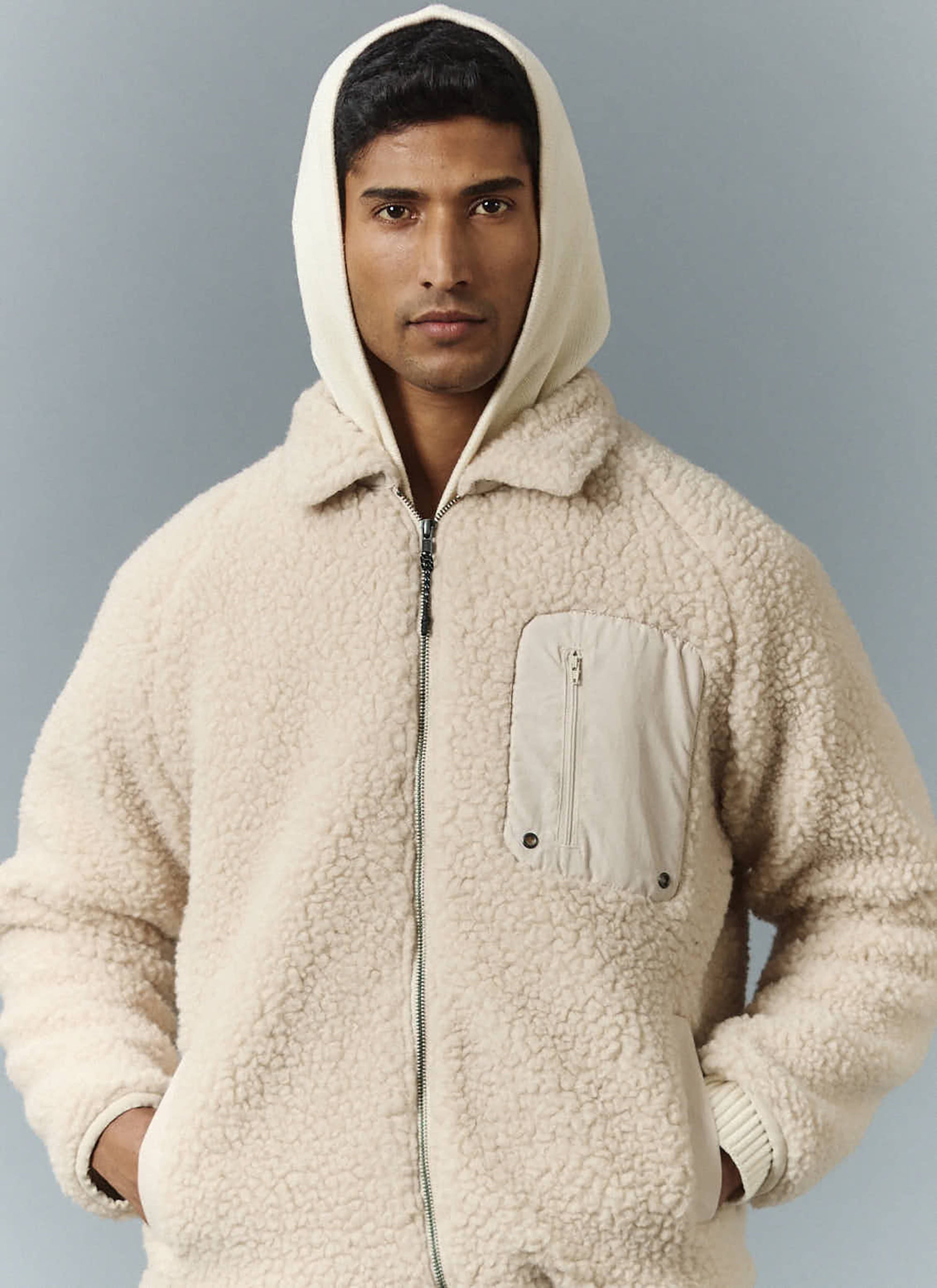 A man models the ecru wool fleece jacket from Percival, layered over a cream hoodie against a plain studio background.