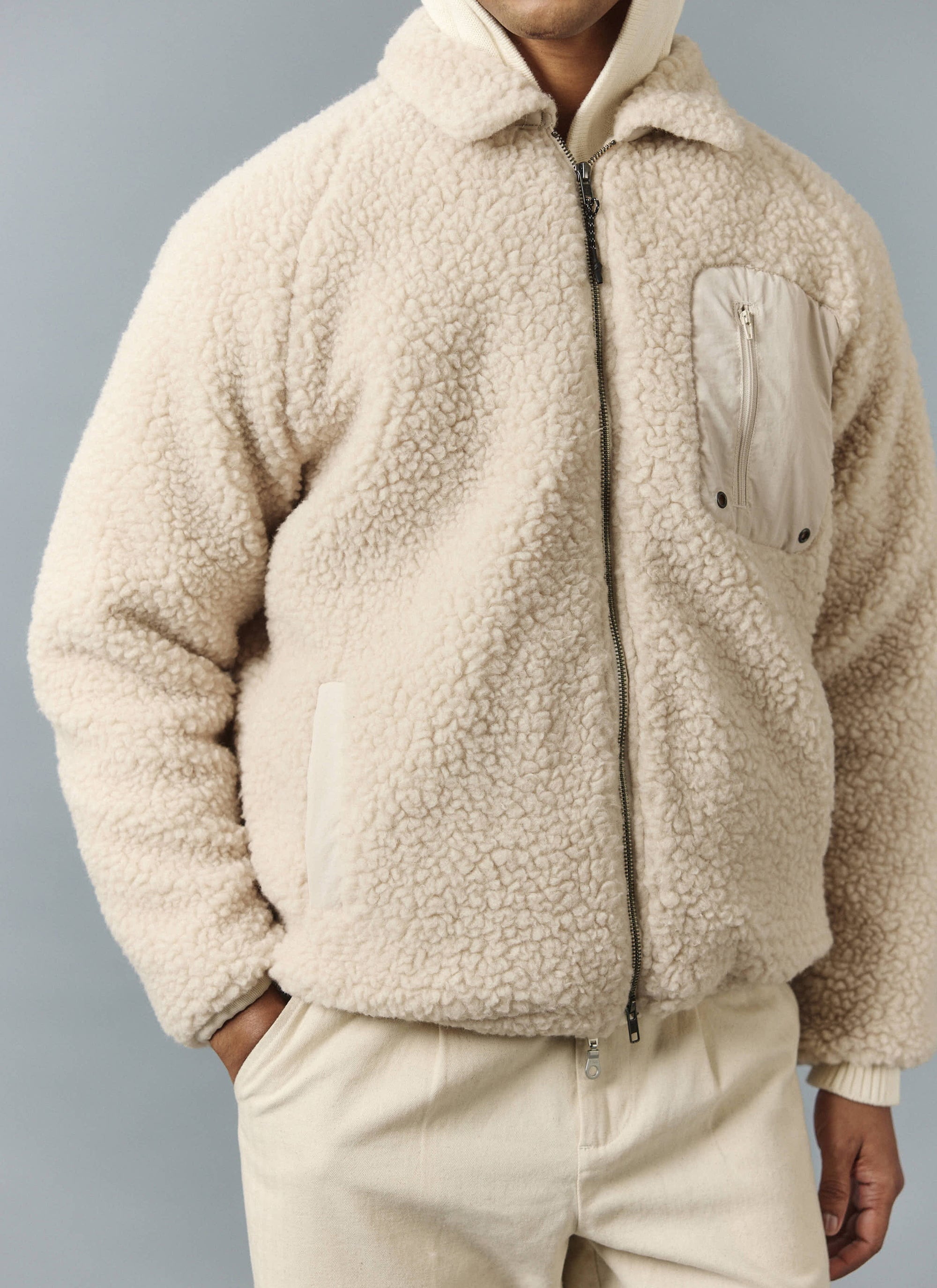 A model wears the Percival Wool Fleece Jacket in ecru, showing the zip-up front, fleece texture, and chest pocket detail.