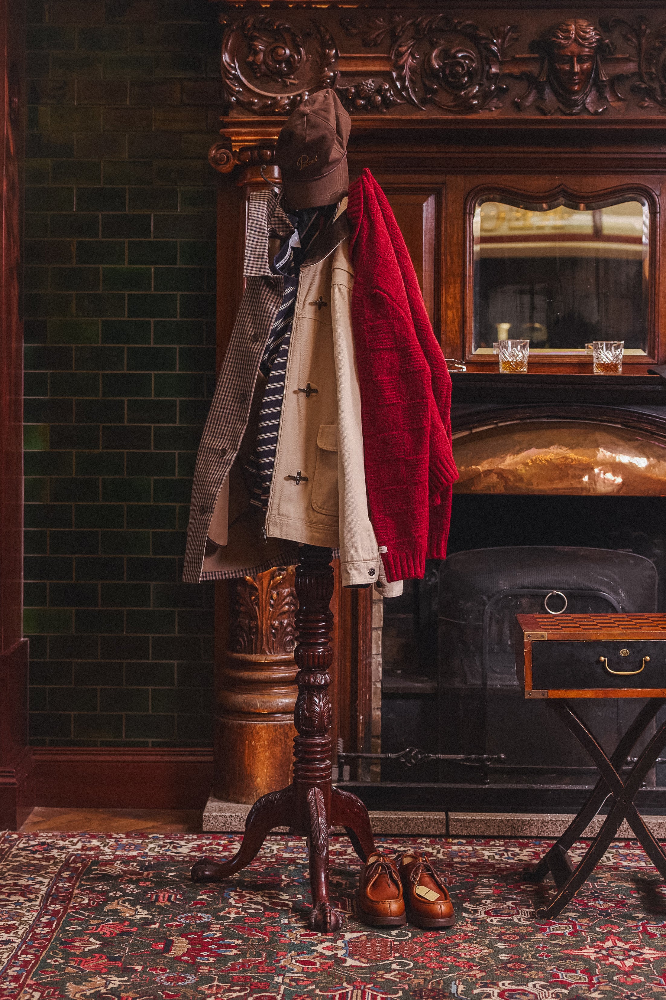 Various Percival garments including a red chunky knit jumper and jackets hanging on a coat stand in a traditional interior.
