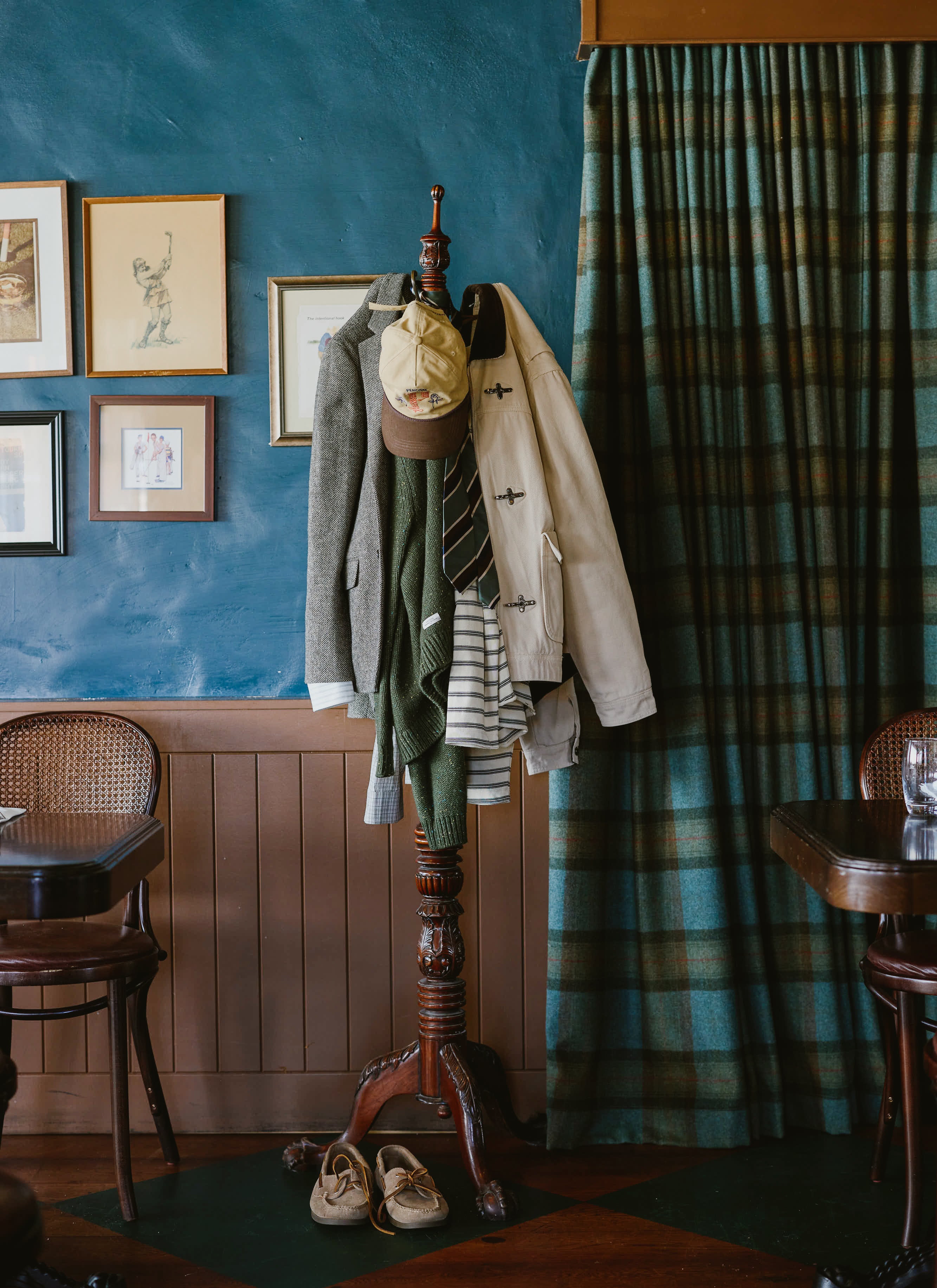 A still life shot displaying various Percival garments and accessories hanging on a vintage wooden coat stand inside a pub.