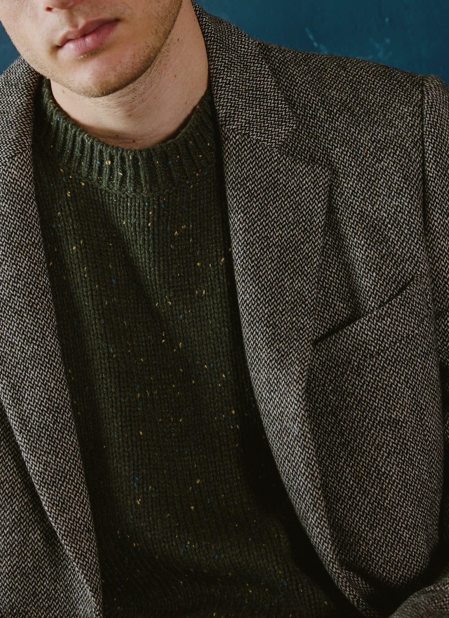 A model wears the Percival forest green Rhodes crew neck jumper layered under a textured blazer.