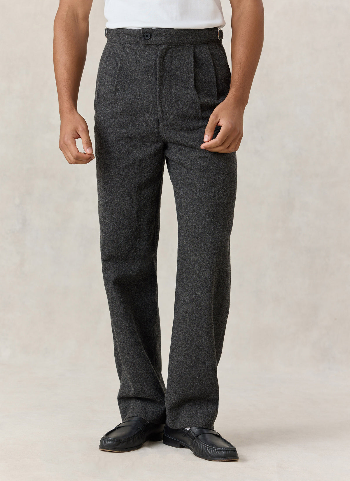 A model wearing the Percival Blake charcoal brushed-wool double-pleated trousers with a white top and black loafers.