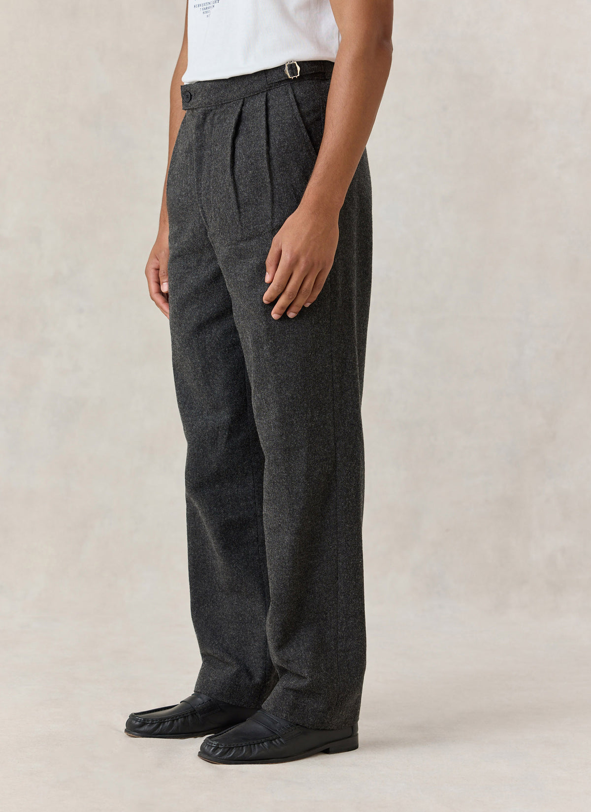 A model wearing Percival Blake charcoal brushed-wool double-pleated tailored trousers with side adjusters and a straight leg.