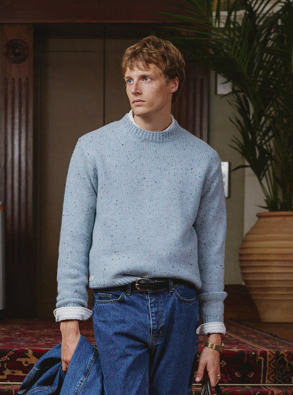 A model wears the blue flecked Percival Rhodes crew neck jumper over a white tee with jeans.