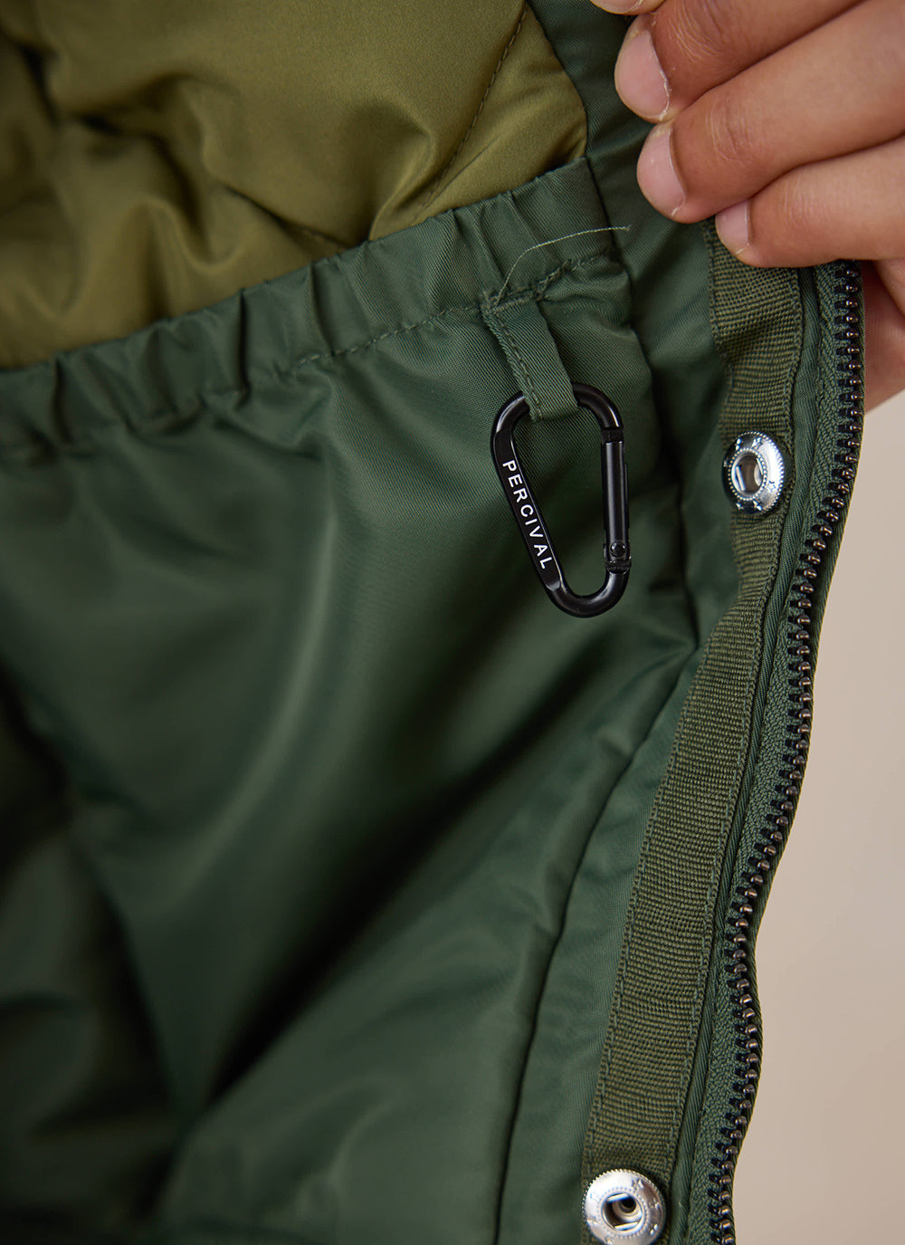 A close-up of the interior lining, hardware and branded carabiner of the forest nylon bomber jacket from Percival.