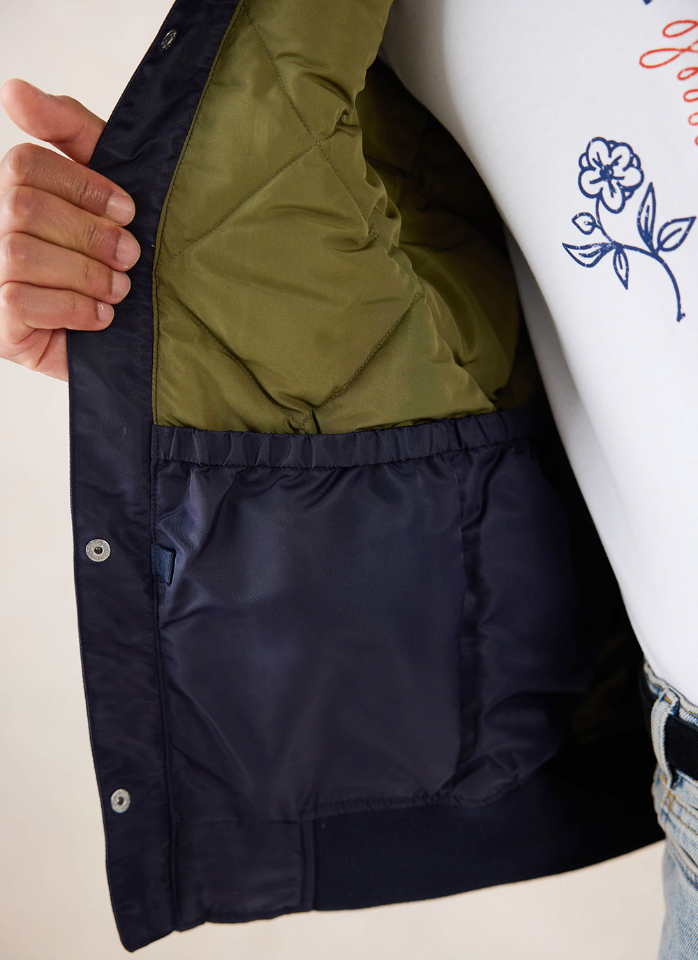 A close-up of the interior quilted olive lining and pocket of the midnight blue nylon bomber jacket from Percival.