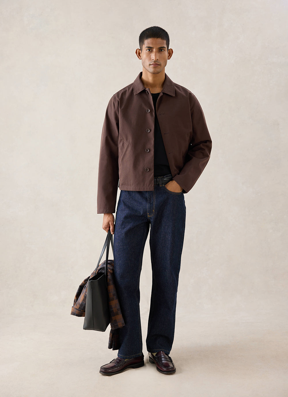 A model wears the espresso Percival Carter Cropped Jacket in a studio, styled with dark jeans, loafers and a tote bag.