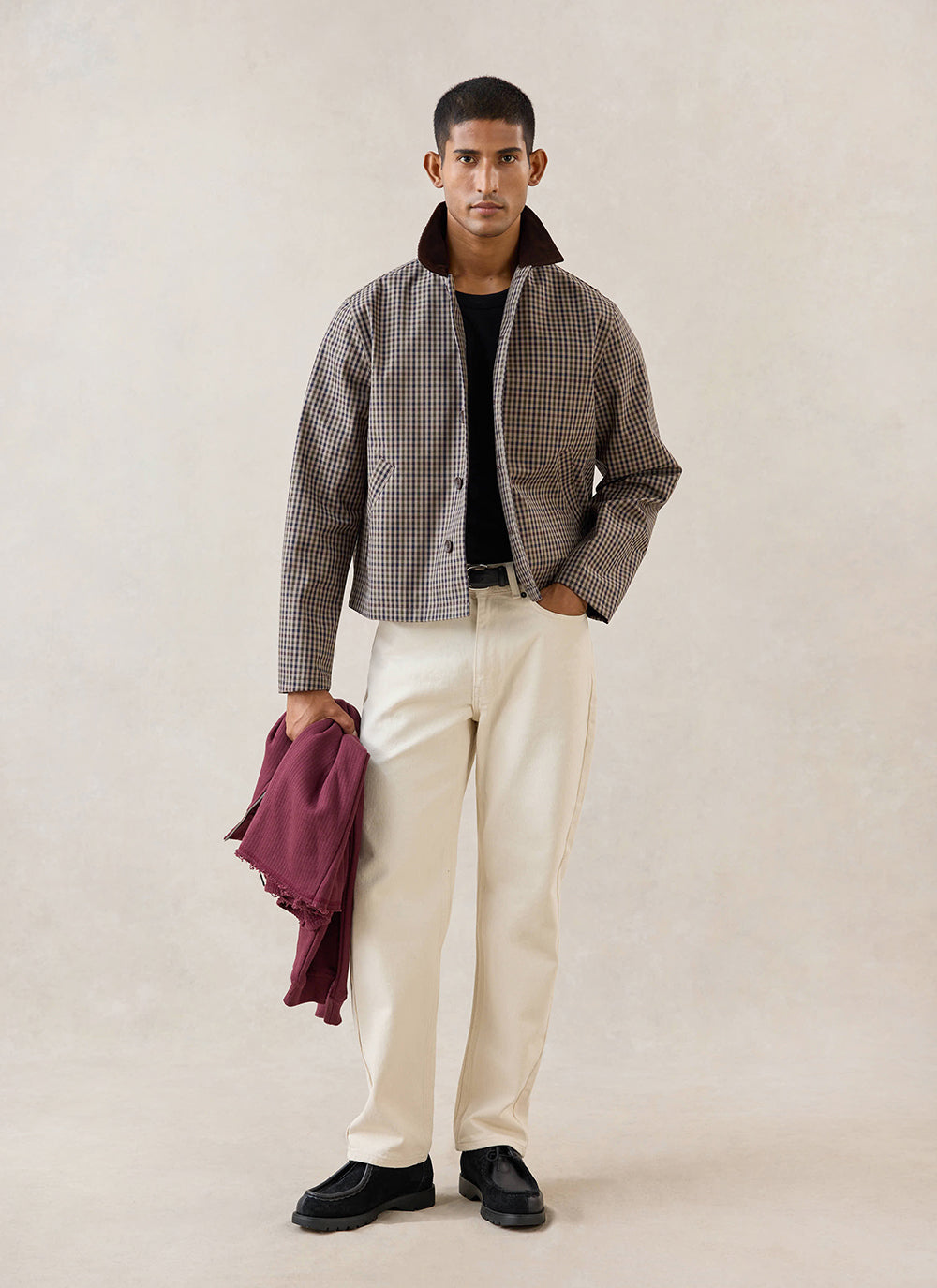 A model wears the Percival Carter Cropped Trench Coat in Watcher Check with white trousers and black shoes in a studio.