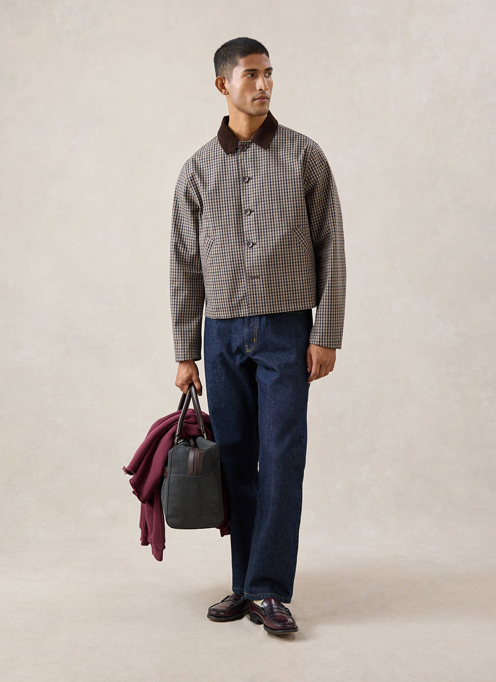 A model wears the waterproof Percival Carter cropped jacket in watcher check, styled with dark denim trousers and a bag.