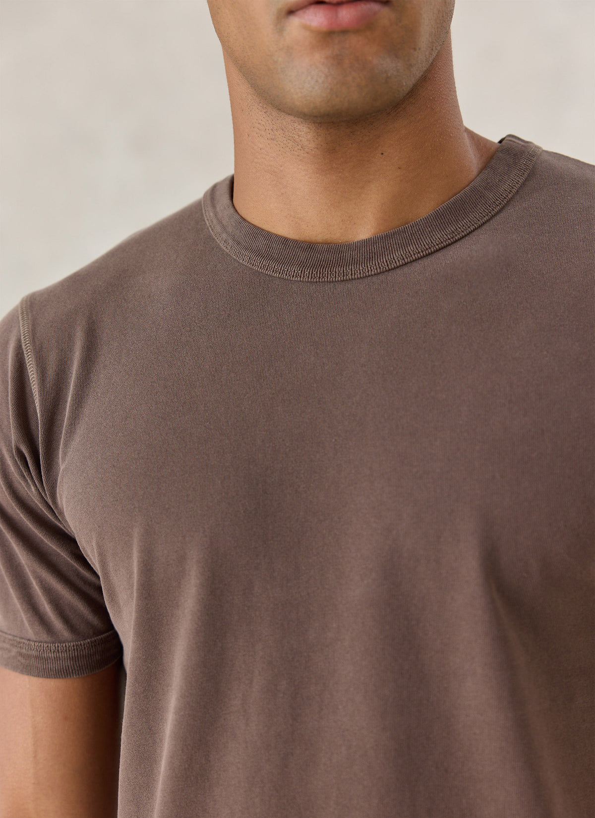Close-up of a model wearing the brown Percival Casey vintage-wash organic cotton T-shirt, highlighting the crew neck.