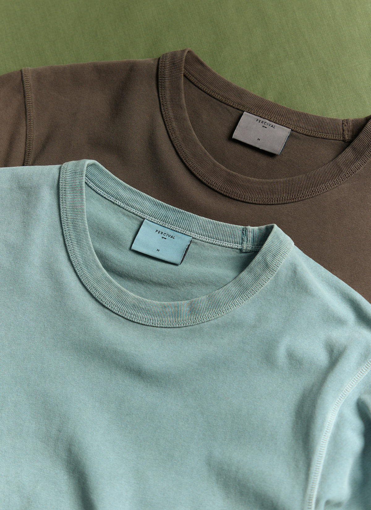A flat lay of Percival Casey vintage wash T-shirts in light blue and brown, highlighting the ribbed crew necks and labels.