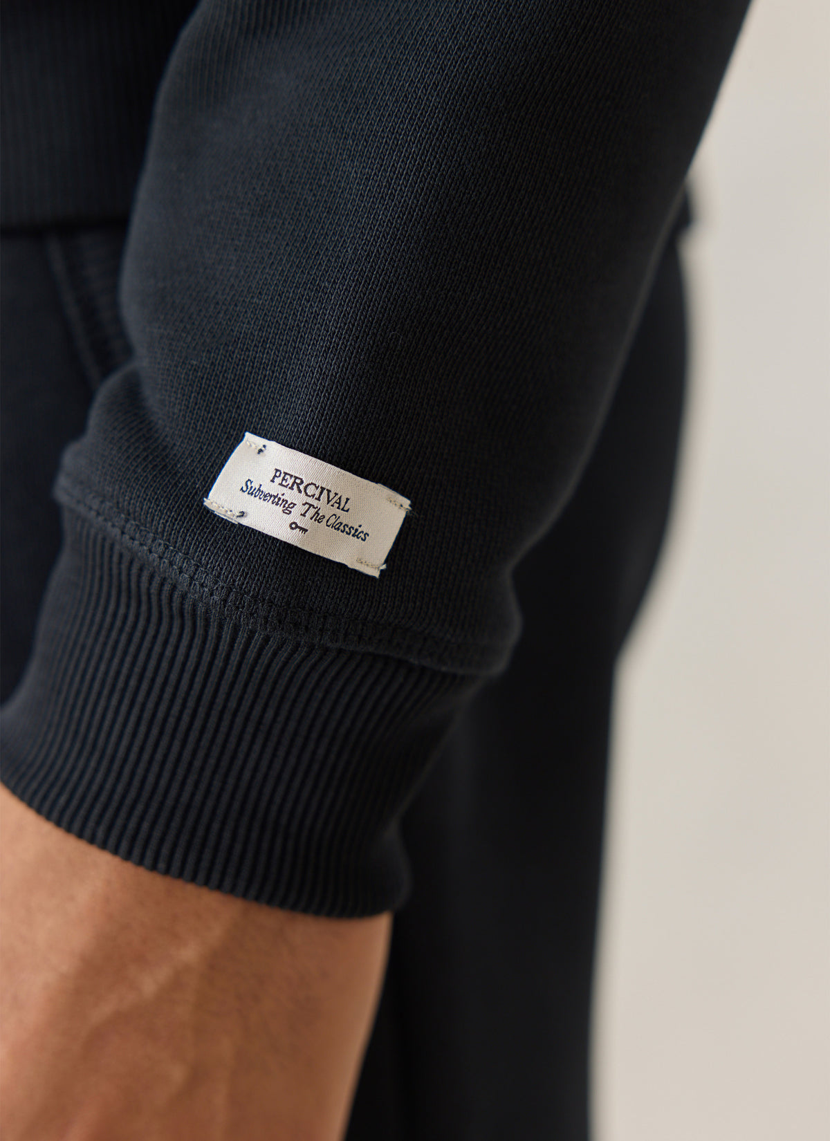 Close-up of the Percival black organic cotton jersey hoodie sleeve showing the ribbed cuff and woven brand label.